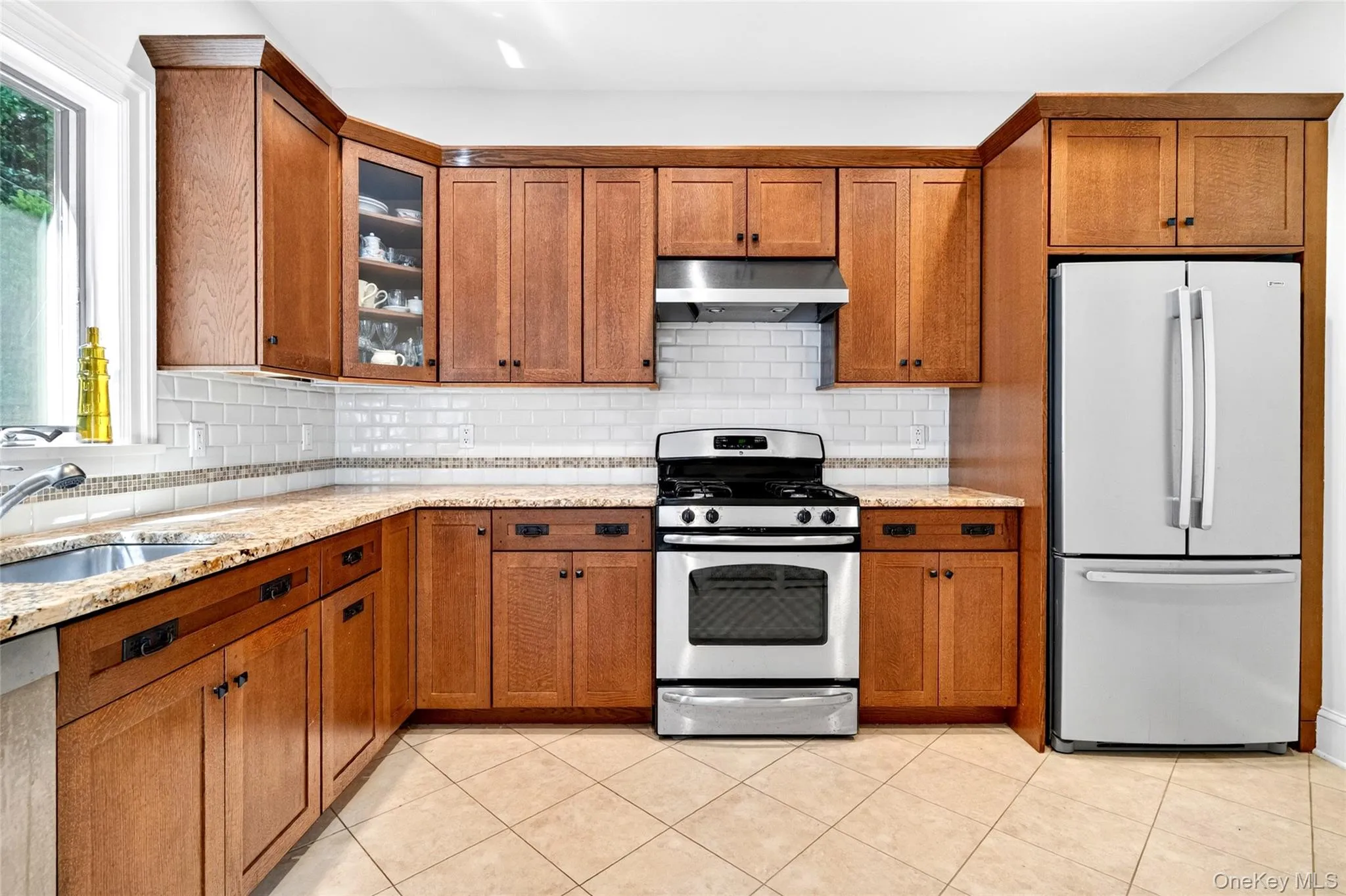 Kitchen featuring wood cabinetry, stainless steel appliances, light-toned countertops, subway tile backsplash, and ceramic tile flooring Kitchen featuring wood cabinetry, stainless steel appliances, light-toned countertops, subway tile backsplash, and ceramic tile flooring