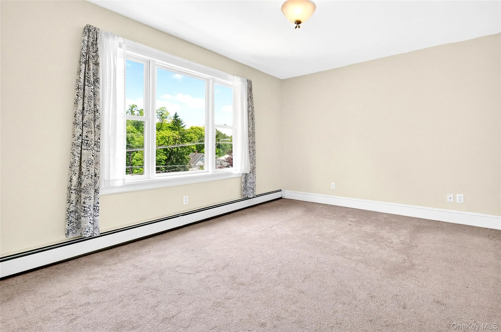 Bright room featuring a multi-pane window, neutral-toned walls, and beige carpeting Bright room featuring a multi-pane window, neutral-toned walls, and beige carpeting