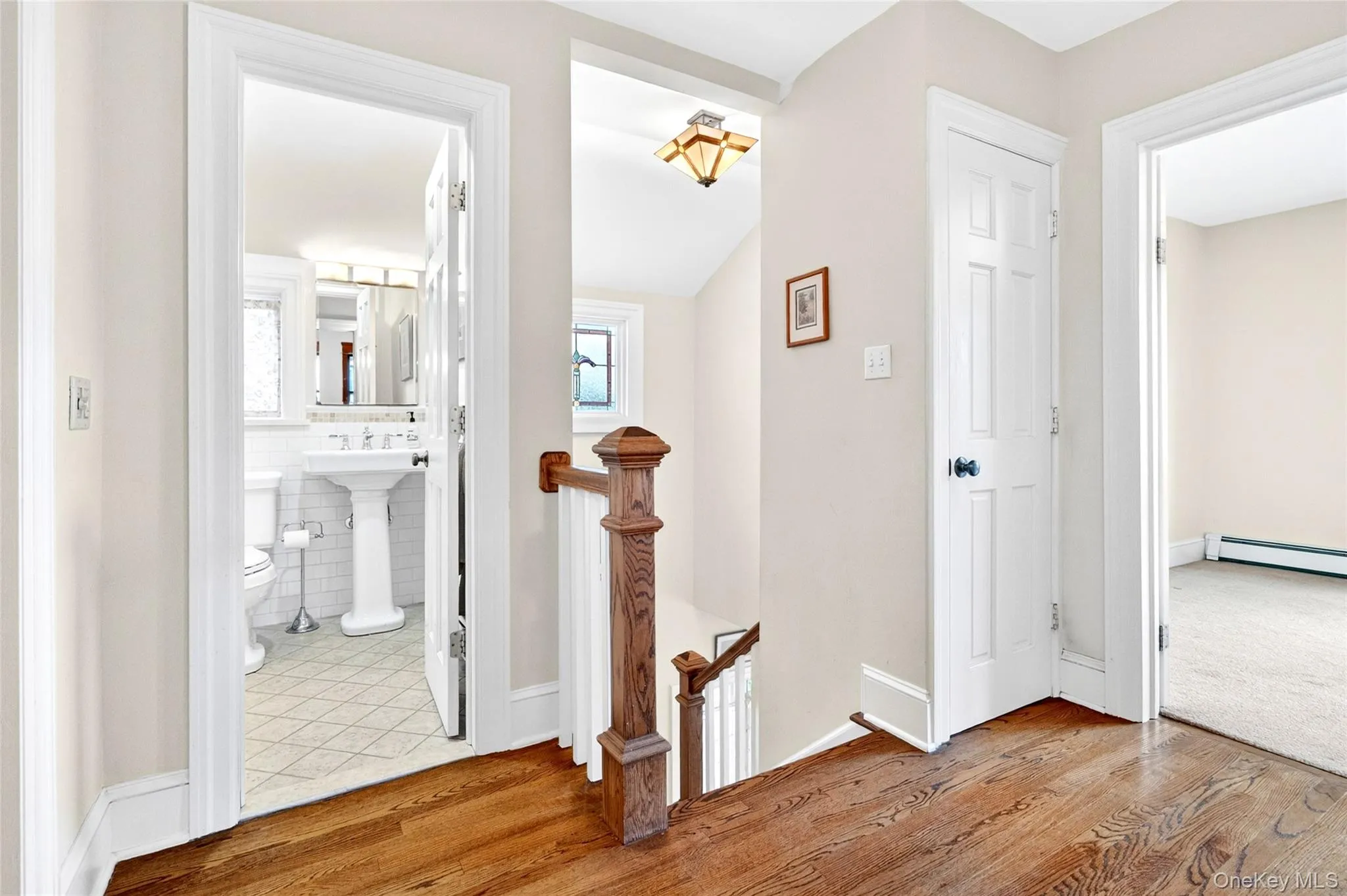 Bright hallway featuring wood-finish flooring, white trim, and a classic wood baluster railing Bright hallway featuring wood-finish flooring, white trim, and a classic wood baluster railing