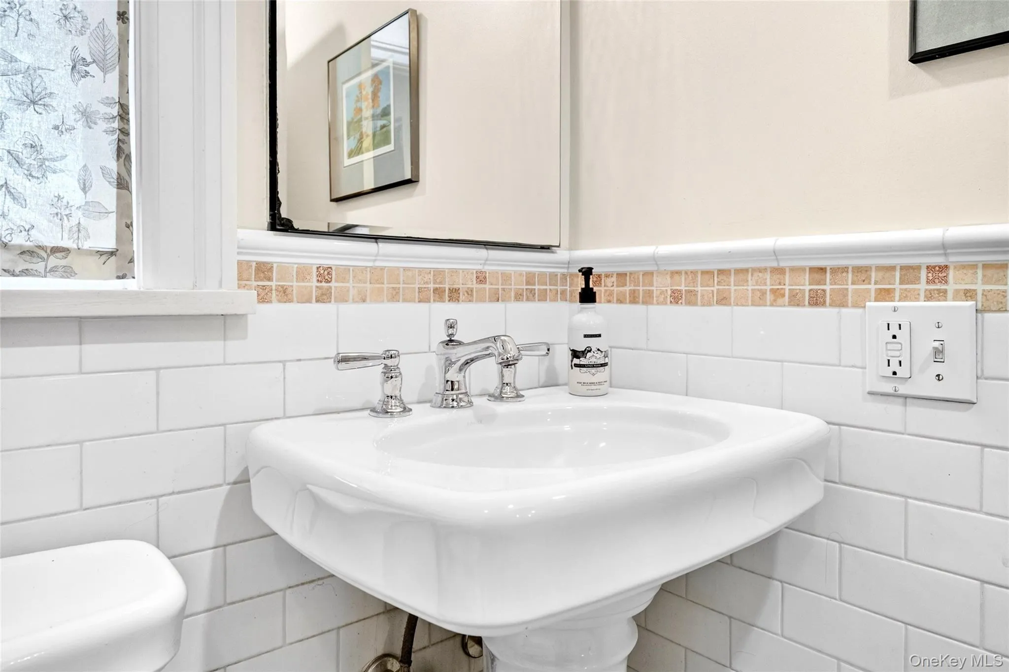 Pedestal sink with chrome faucet, white subway tile wainscoting, and mosaic tile accent Pedestal sink with chrome faucet, white subway tile wainscoting, and mosaic tile accent