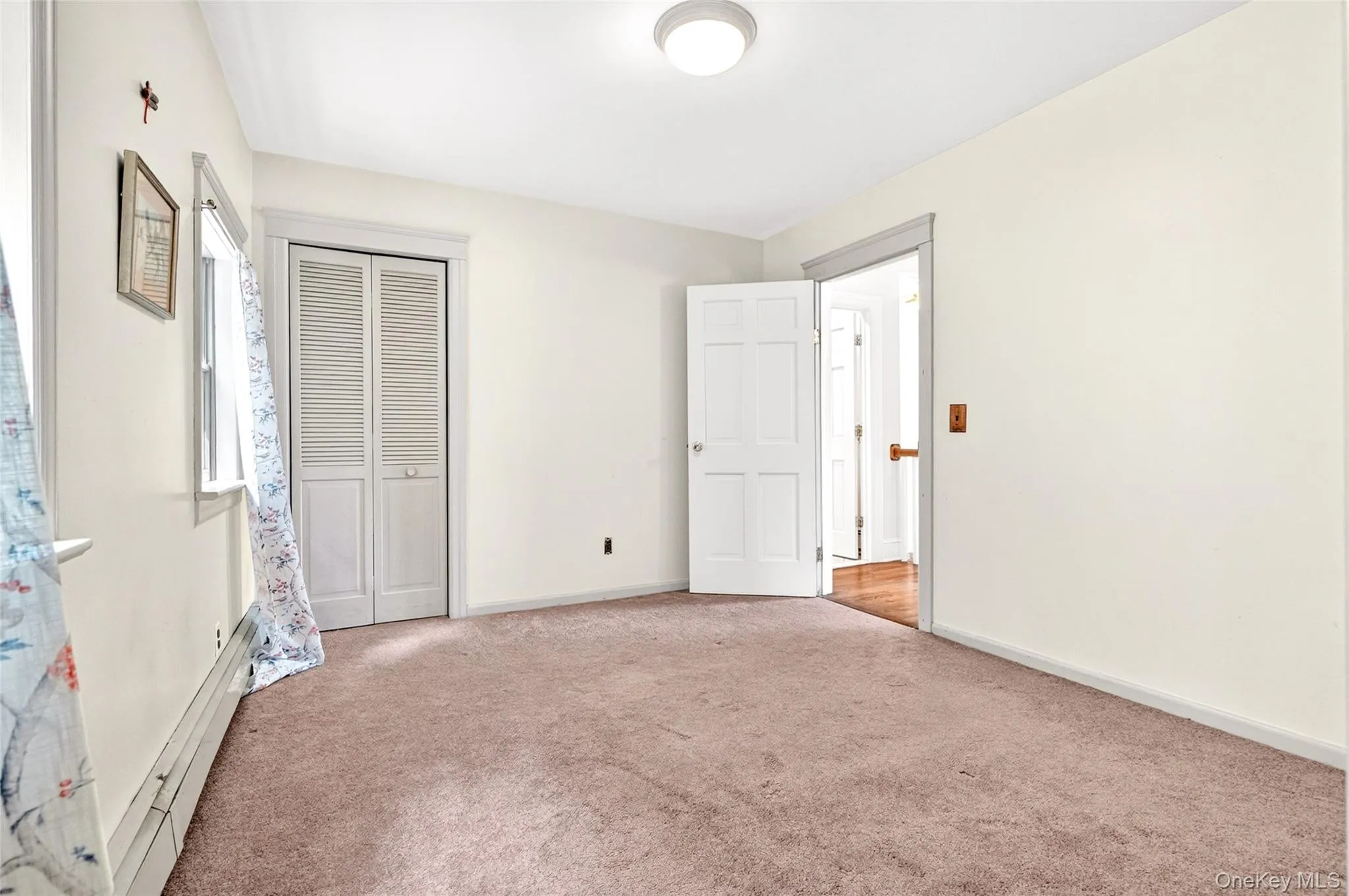 Carpeted room featuring a ceiling-mounted light fixture, white walls, and a louvered bi-fold closet door Carpeted room featuring a ceiling-mounted light fixture, white walls, and a louvered bi-fold closet door