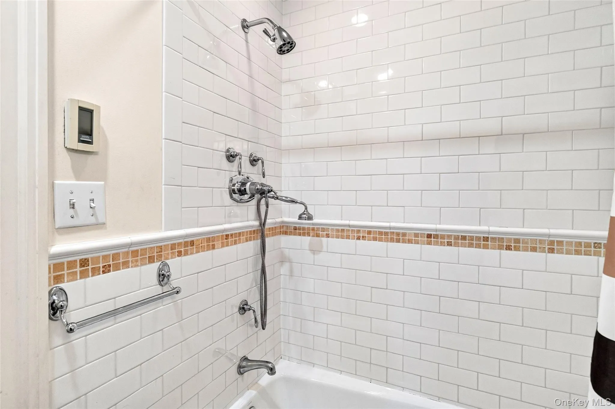 Bathtub and shower combination featuring subway tile surround, decorative mosaic tile accent band, and chrome fixtures Bathtub and shower combination featuring subway tile surround, decorative mosaic tile accent band, and chrome fixtures