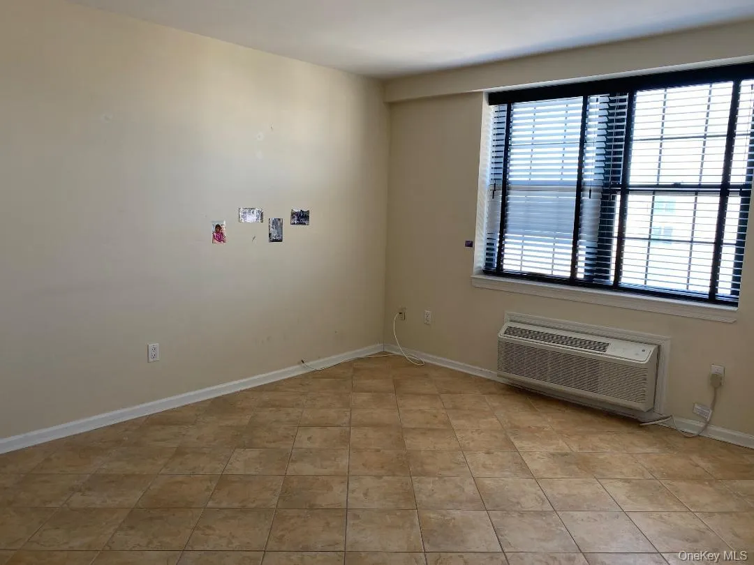 Unfurnished room with light tile patterned floors, baseboards, and a wall mounted air conditioner Unfurnished room with light tile patterned floors, baseboards, and a wall mounted air conditioner