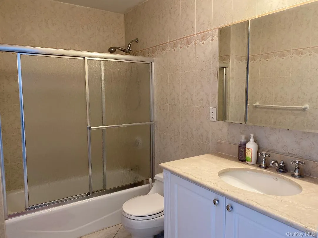 Full bathroom with enclosed tub / shower combo, toilet, vanity, tile walls, and tile patterned floors Full bathroom with enclosed tub / shower combo, toilet, vanity, tile walls, and tile patterned floors