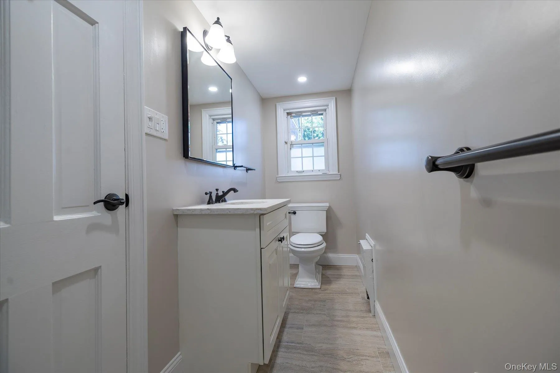 Bathroom featuring a white vanity with countertop, dark-finish faucet, and rectangular mirror with a three-light fixture. Bathroom featuring a white vanity with countertop, dark-finish faucet, and rectangular mirror with a three-light fixture.