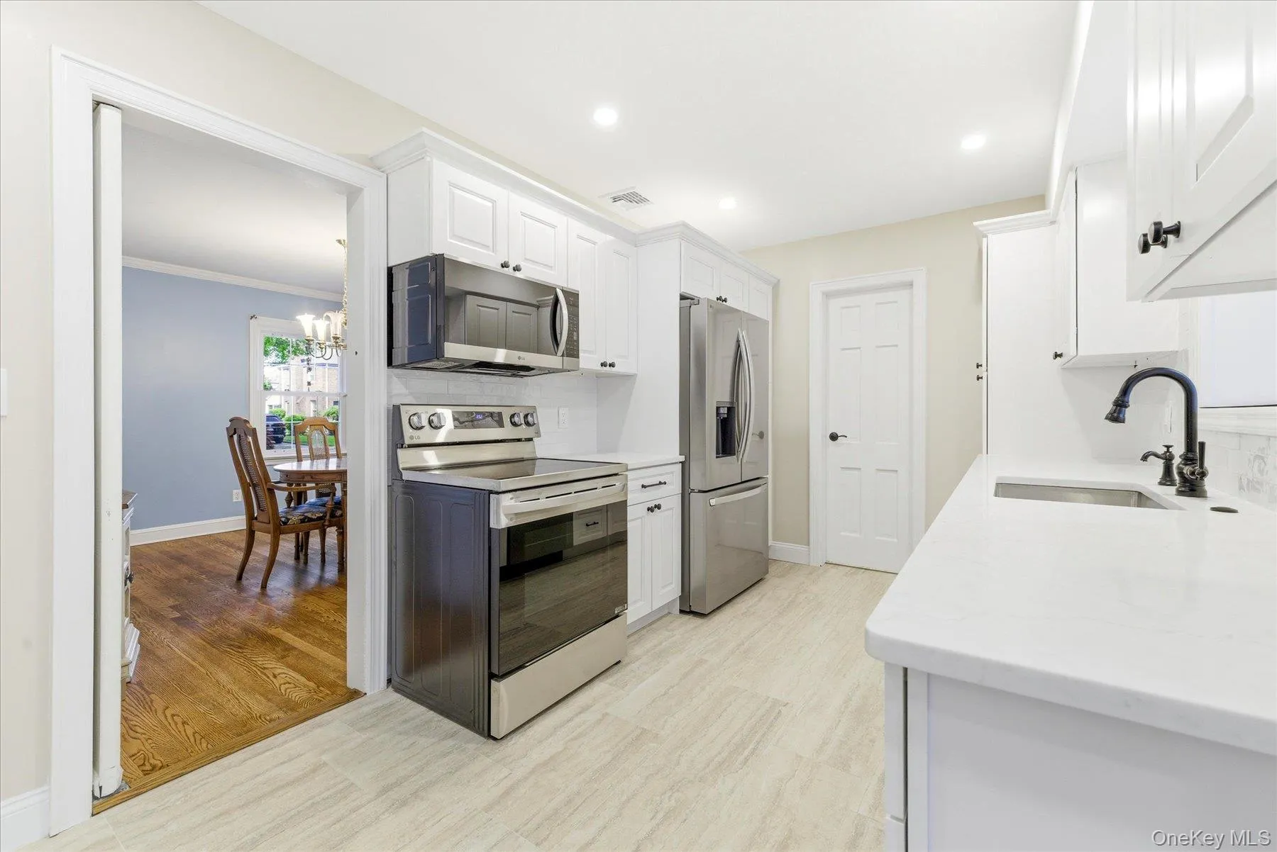 Modern kitchen featuring white shaker cabinetry, stainless steel appliances, light-toned tile flooring, and white countertops Modern kitchen featuring white shaker cabinetry, stainless steel appliances, light-toned tile flooring, and white countertops