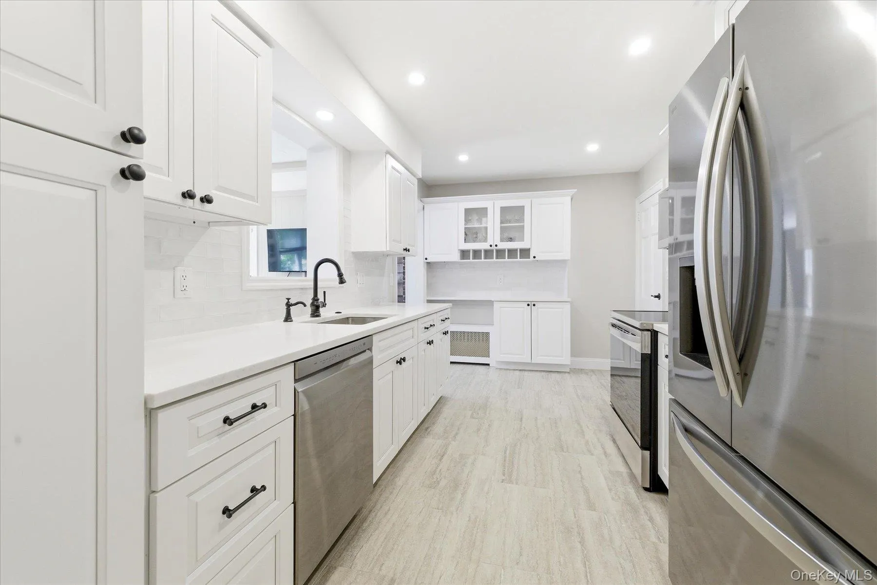 Kitchen featuring white shaker-style cabinetry, stainless steel appliances, a matte black faucet, light-toned tile flooring, and recessed lighting Kitchen featuring white shaker-style cabinetry, stainless steel appliances, a matte black faucet, light-toned tile flooring, and recessed lighting