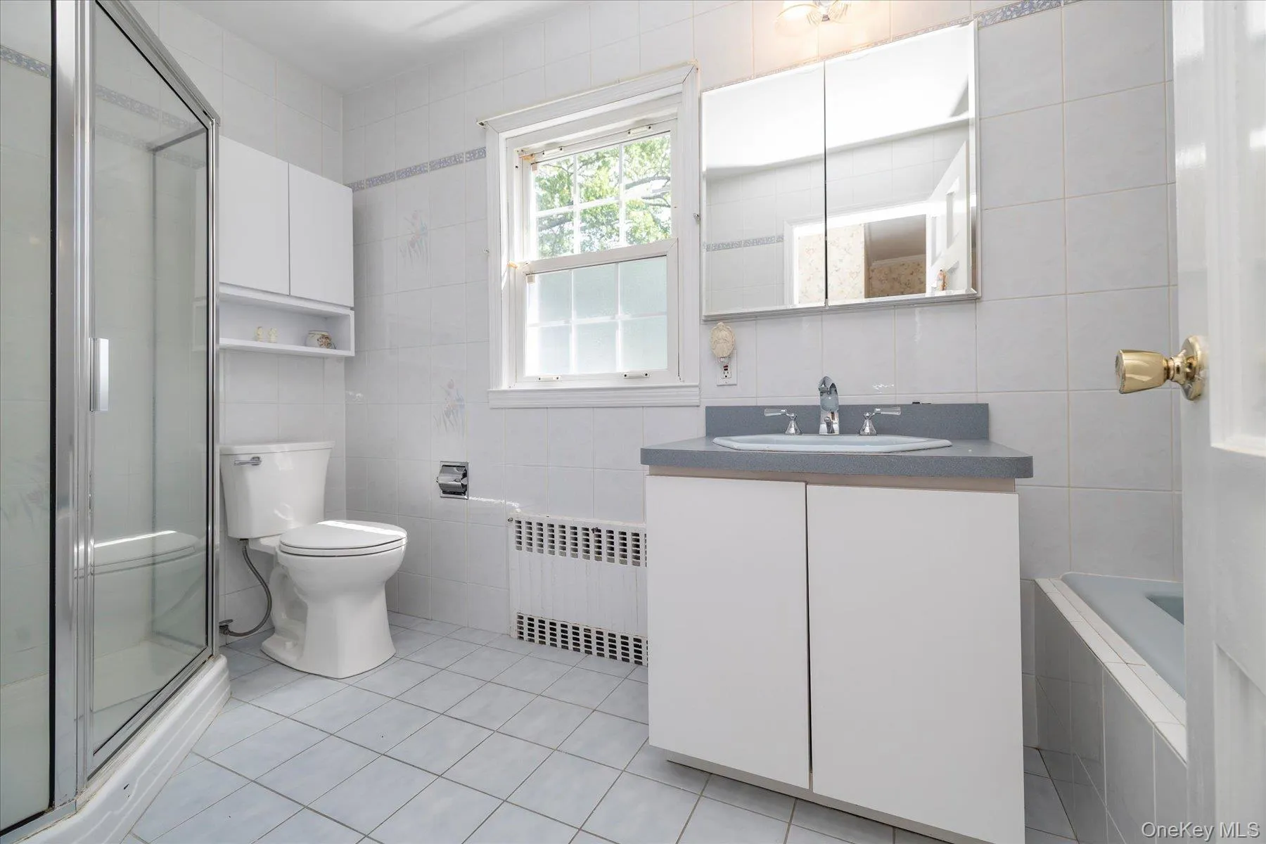 Full bathroom featuring a tile shower enclosure, light blue tile flooring, a window, a white vanity with a gray countertop and integrated sink, and a mirrored medicine cabinet. Full bathroom featuring a tile shower enclosure, light blue tile flooring, a window, a white vanity with a gray countertop and integrated sink, and a mirrored medicine cabinet.
