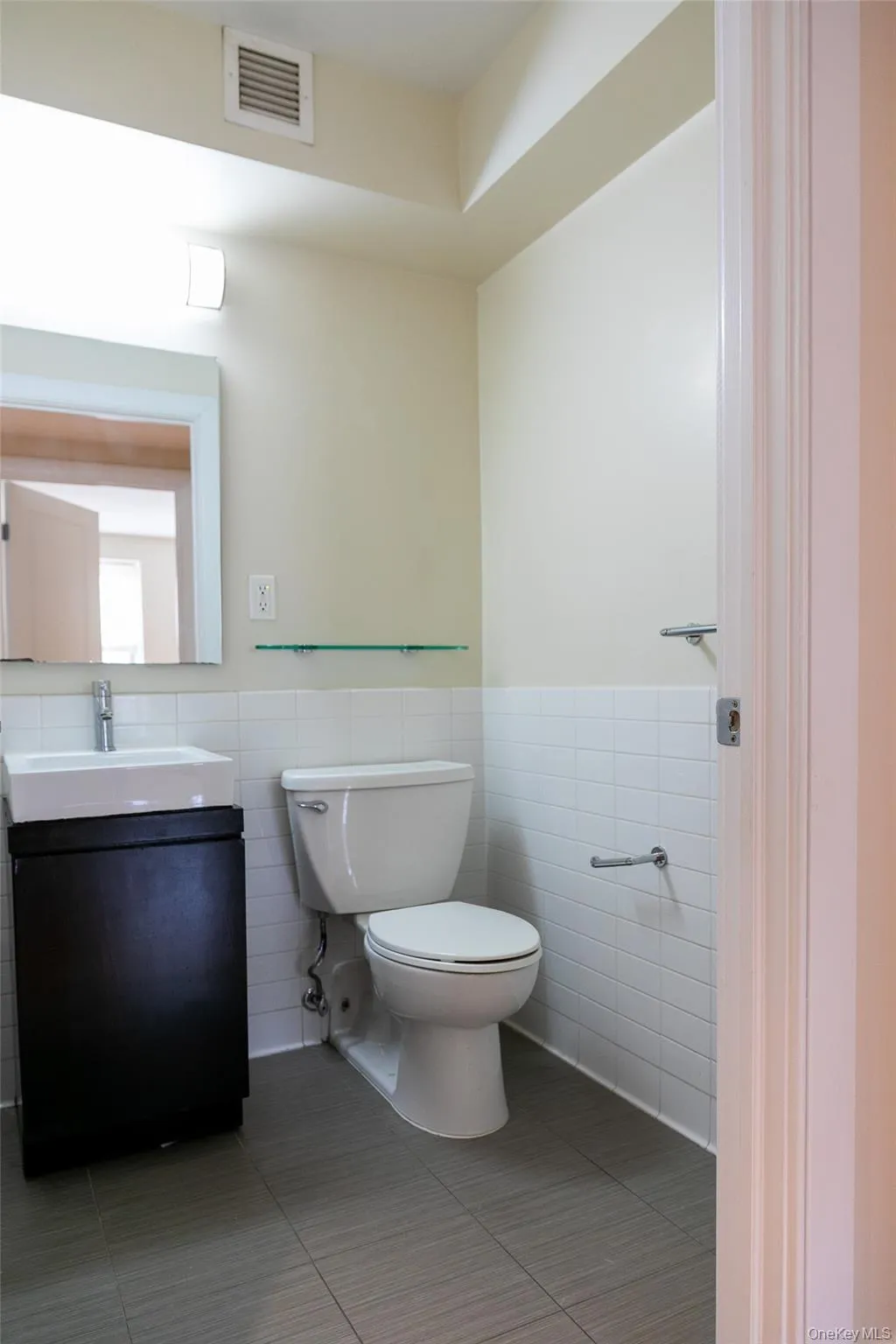 Bathroom featuring a contemporary vanity with an integrated sink, white subway tile wainscoting, and a wall-mounted mirror Bathroom featuring a contemporary vanity with an integrated sink, white subway tile wainscoting, and a wall-mounted mirror