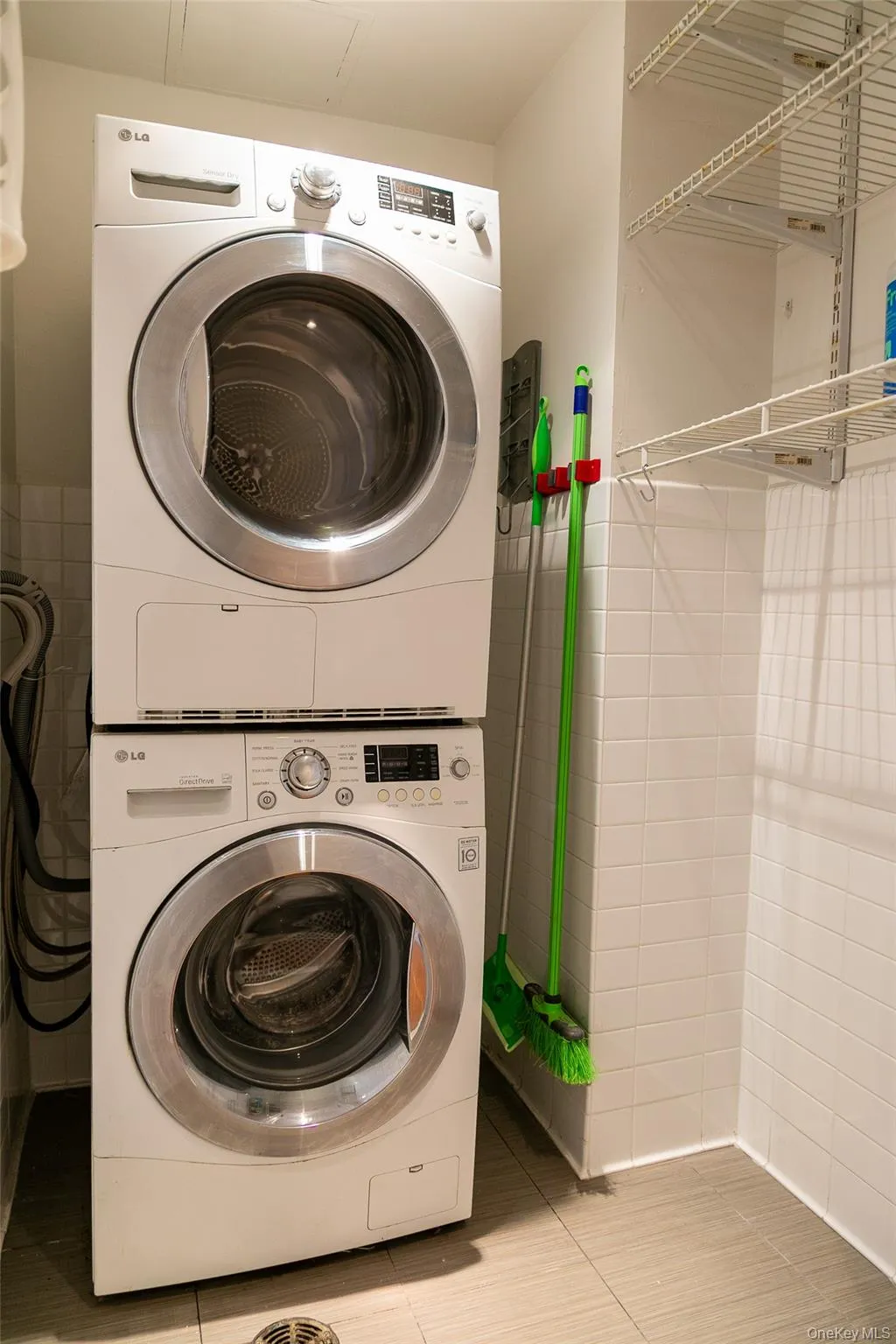 Dedicated laundry area featuring a stacked washer and dryer, tiled walls, wire shelving, and neutral-toned flooring Dedicated laundry area featuring a stacked washer and dryer, tiled walls, wire shelving, and neutral-toned flooring
