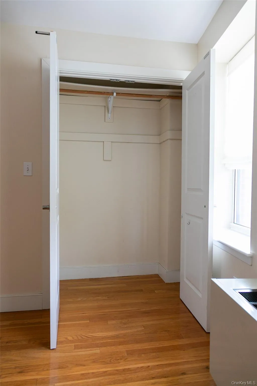 Spacious closet featuring bi-fold doors, wood-finish flooring, and a built-in hanging rod Spacious closet featuring bi-fold doors, wood-finish flooring, and a built-in hanging rod