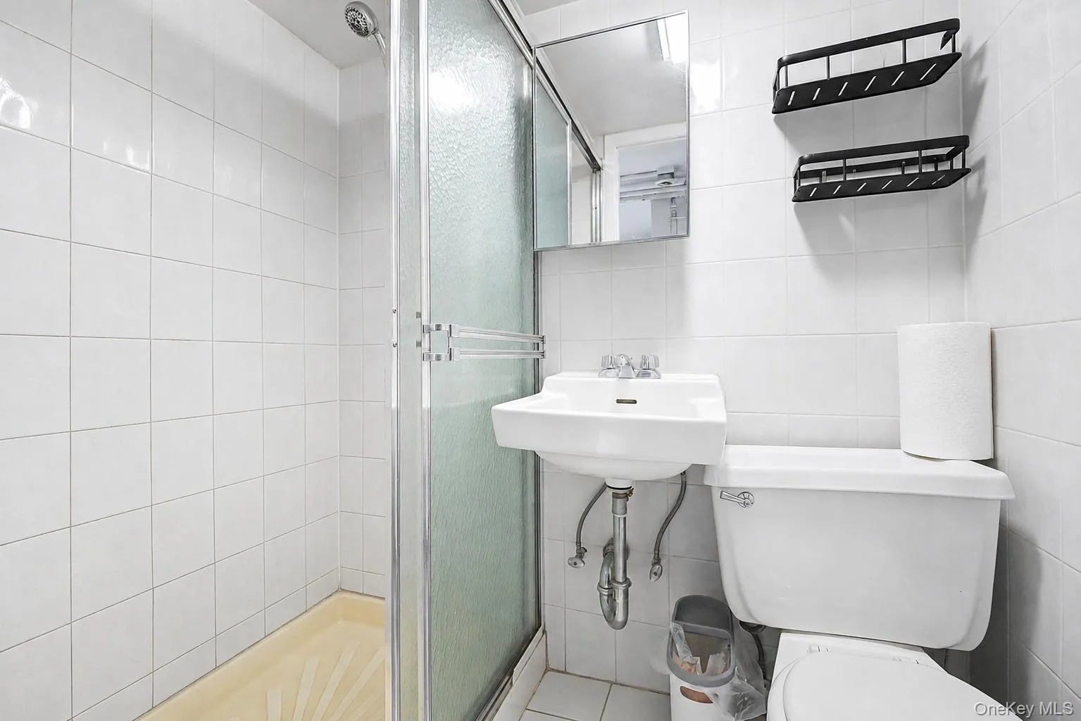 Compact bathroom featuring a shower enclosure with frosted glass, a wall-mounted sink, and a toilet Compact bathroom featuring a shower enclosure with frosted glass, a wall-mounted sink, and a toilet