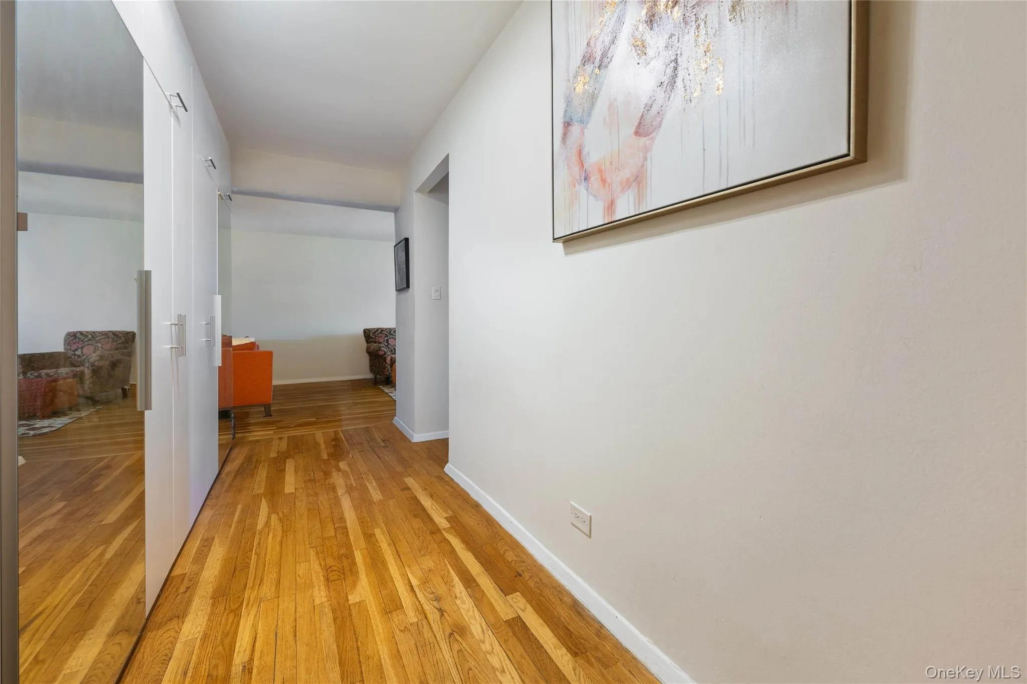 Hallway featuring wood-finish flooring, white walls, and built-in mirrored closet doors with brushed nickel hardware Hallway featuring wood-finish flooring, white walls, and built-in mirrored closet doors with brushed nickel hardware