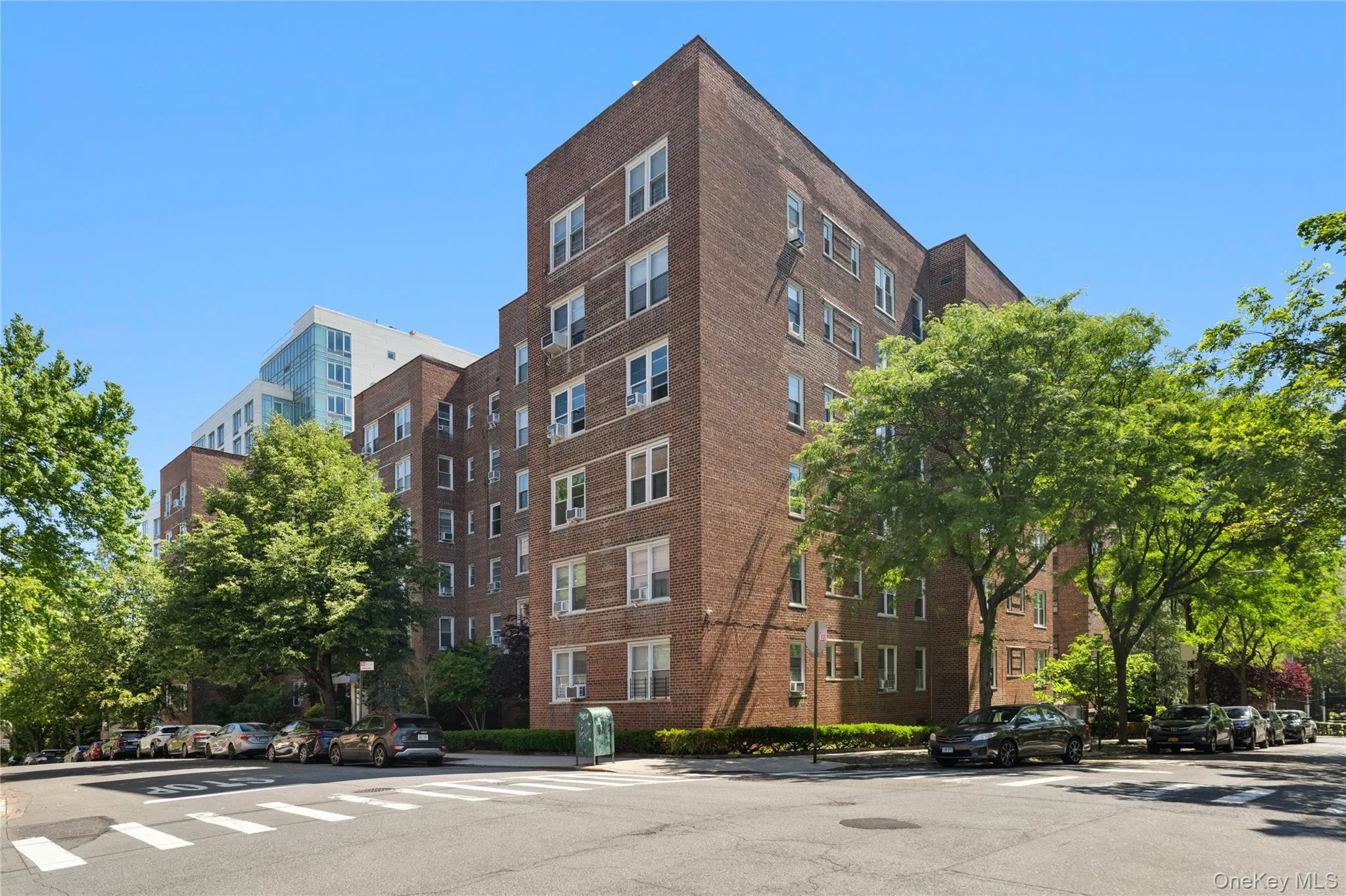 Multi-story brick facade building featuring numerous windows, a street-level entrance, and established perimeter trees Multi-story brick facade building featuring numerous windows, a street-level entrance, and established perimeter trees