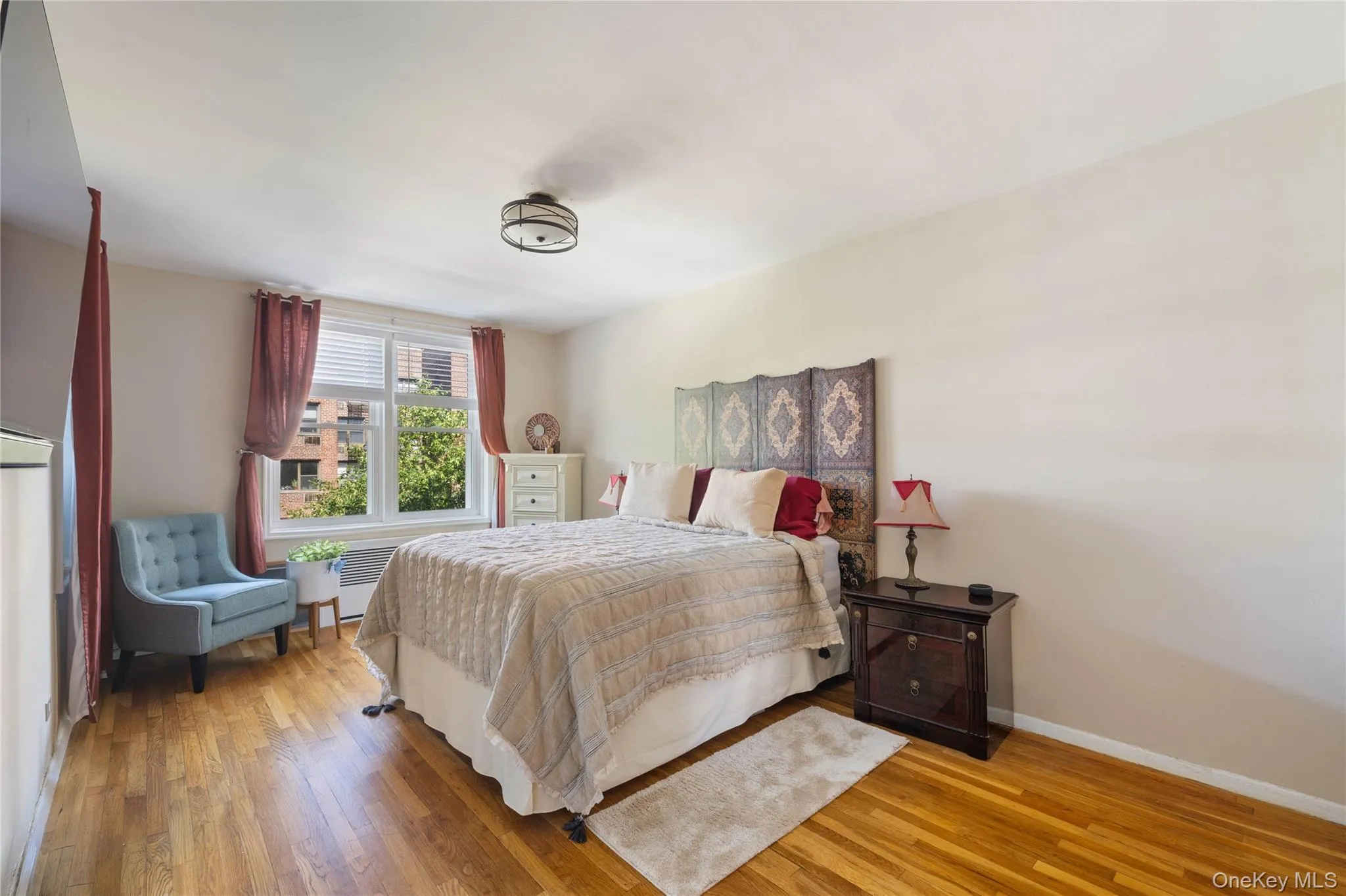 Bedroom featuring wood-finish flooring, a window with blinds, and a ceiling-mounted light fixture Bedroom featuring wood-finish flooring, a window with blinds, and a ceiling-mounted light fixture