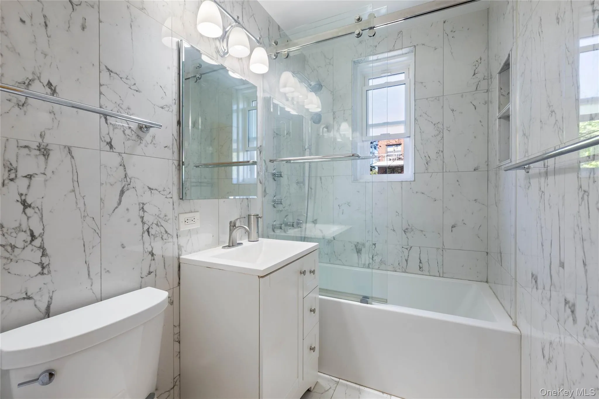 Full bathroom featuring floor-to-ceiling white marble-look tiling Full bathroom featuring floor-to-ceiling white marble-look tiling