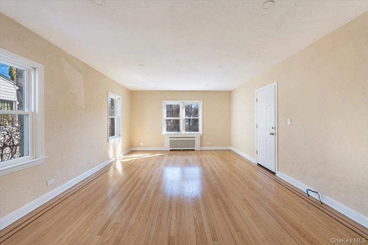 Unfurnished room with light wood-type flooring, radiator, and baseboards Unfurnished room with light wood-type flooring, radiator, and baseboards