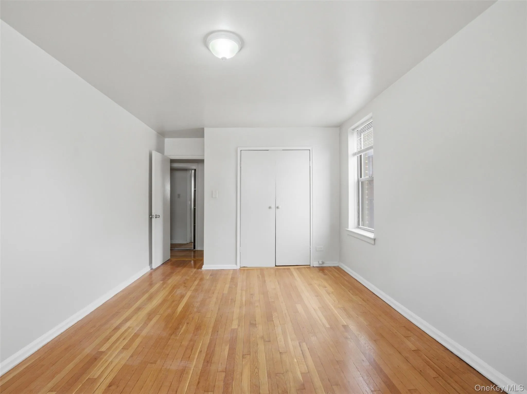 Hardwood flooring throughout, featuring a double-door closet and a single window with vertical muntins Hardwood flooring throughout, featuring a double-door closet and a single window with vertical muntins