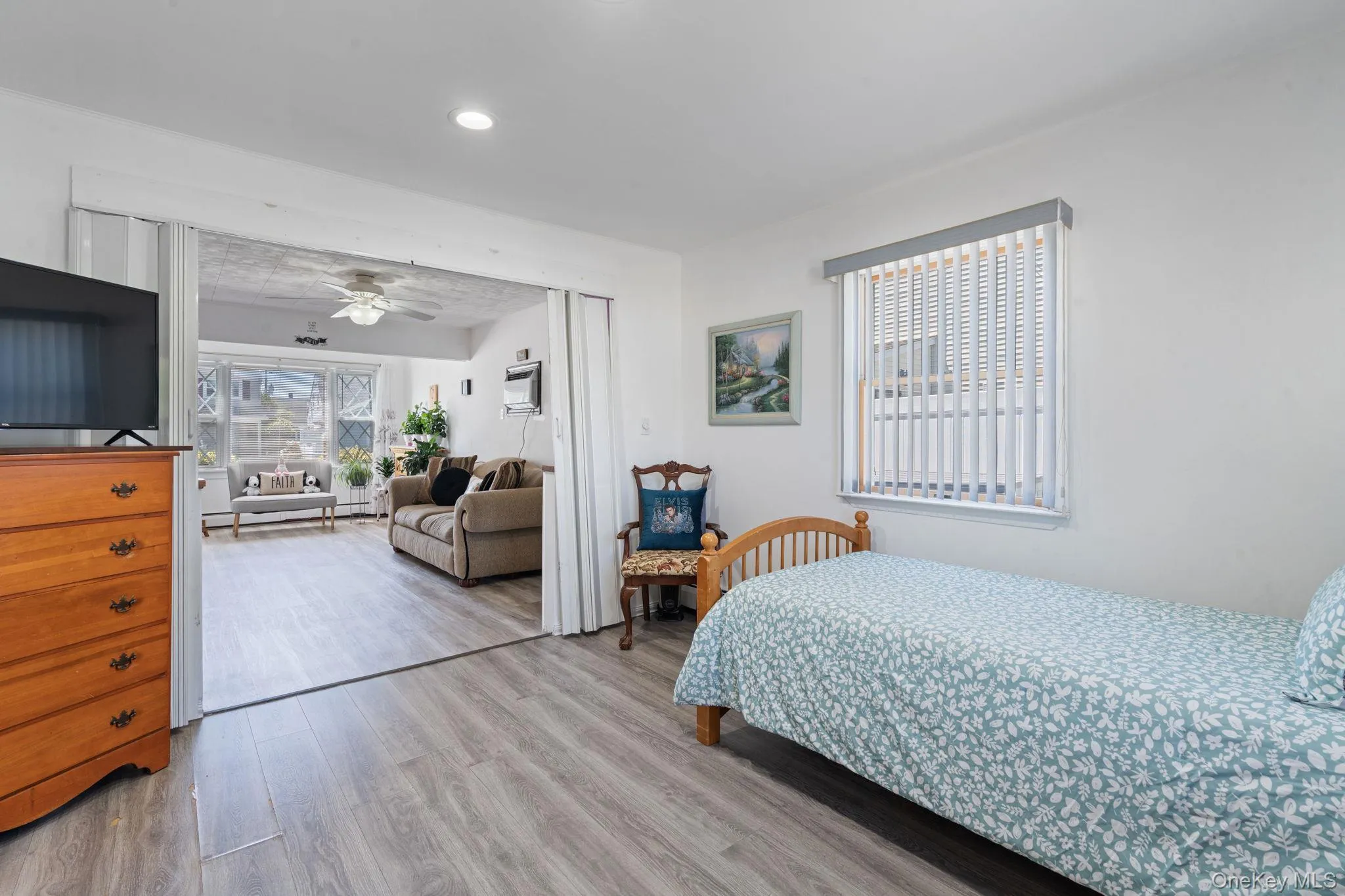 Spacious room featuring wood-finish flooring and a large window with vertical blinds Spacious room featuring wood-finish flooring and a large window with vertical blinds