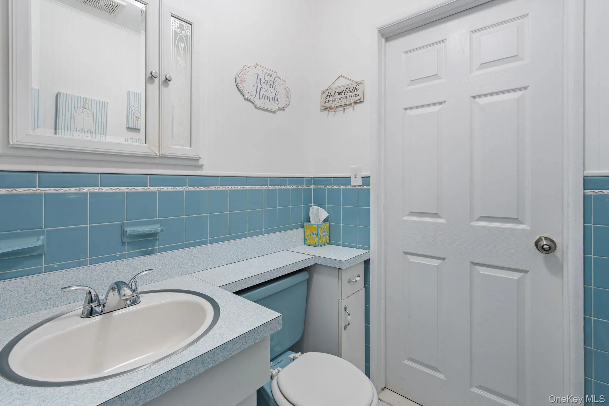 Bathroom featuring a vanity with an integrated sink, chrome faucet, and blue tiled wainscoting Bathroom featuring a vanity with an integrated sink, chrome faucet, and blue tiled wainscoting