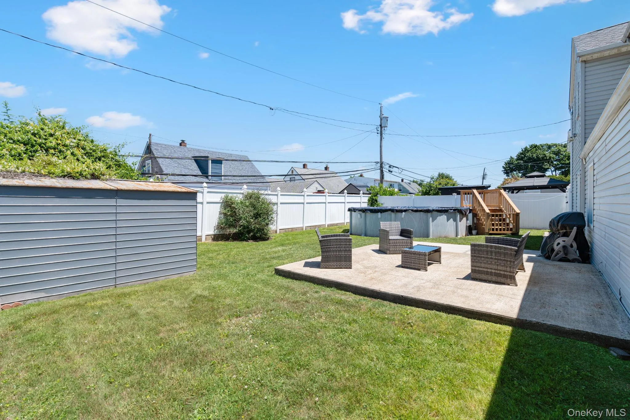 Expansive backyard featuring a concrete patio, a detached storage shed, a vinyl fence, and a partially recessed above-ground pool with wood stairs Expansive backyard featuring a concrete patio, a detached storage shed, a vinyl fence, and a partially recessed above-ground pool with wood stairs