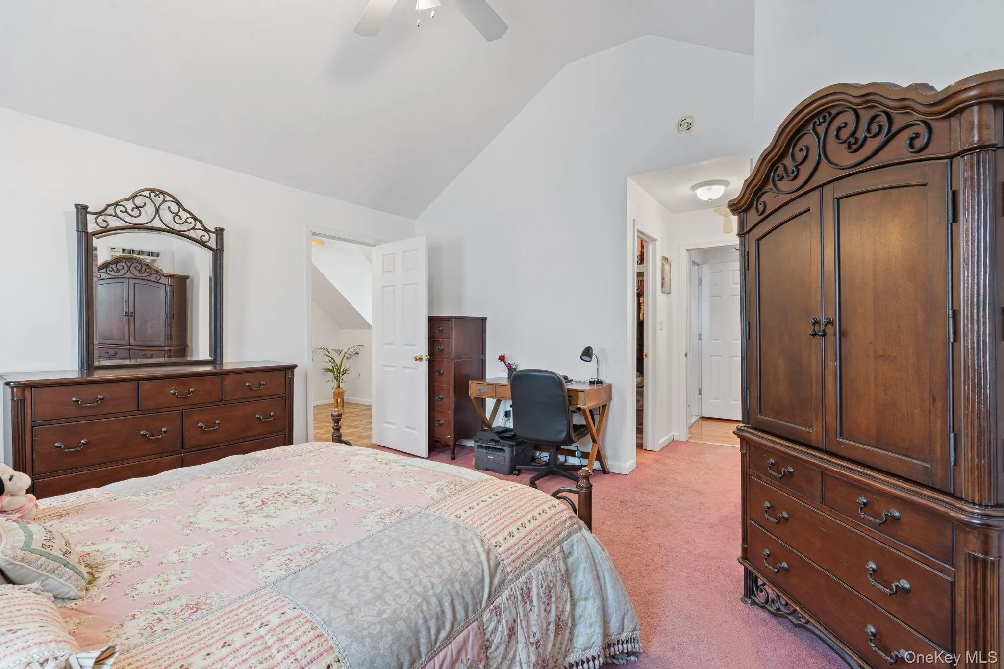 Room featuring a vaulted ceiling with a ceiling fan, a doorway leading to a staircase, and a hallway entrance with wood-finish flooring Room featuring a vaulted ceiling with a ceiling fan, a doorway leading to a staircase, and a hallway entrance with wood-finish flooring