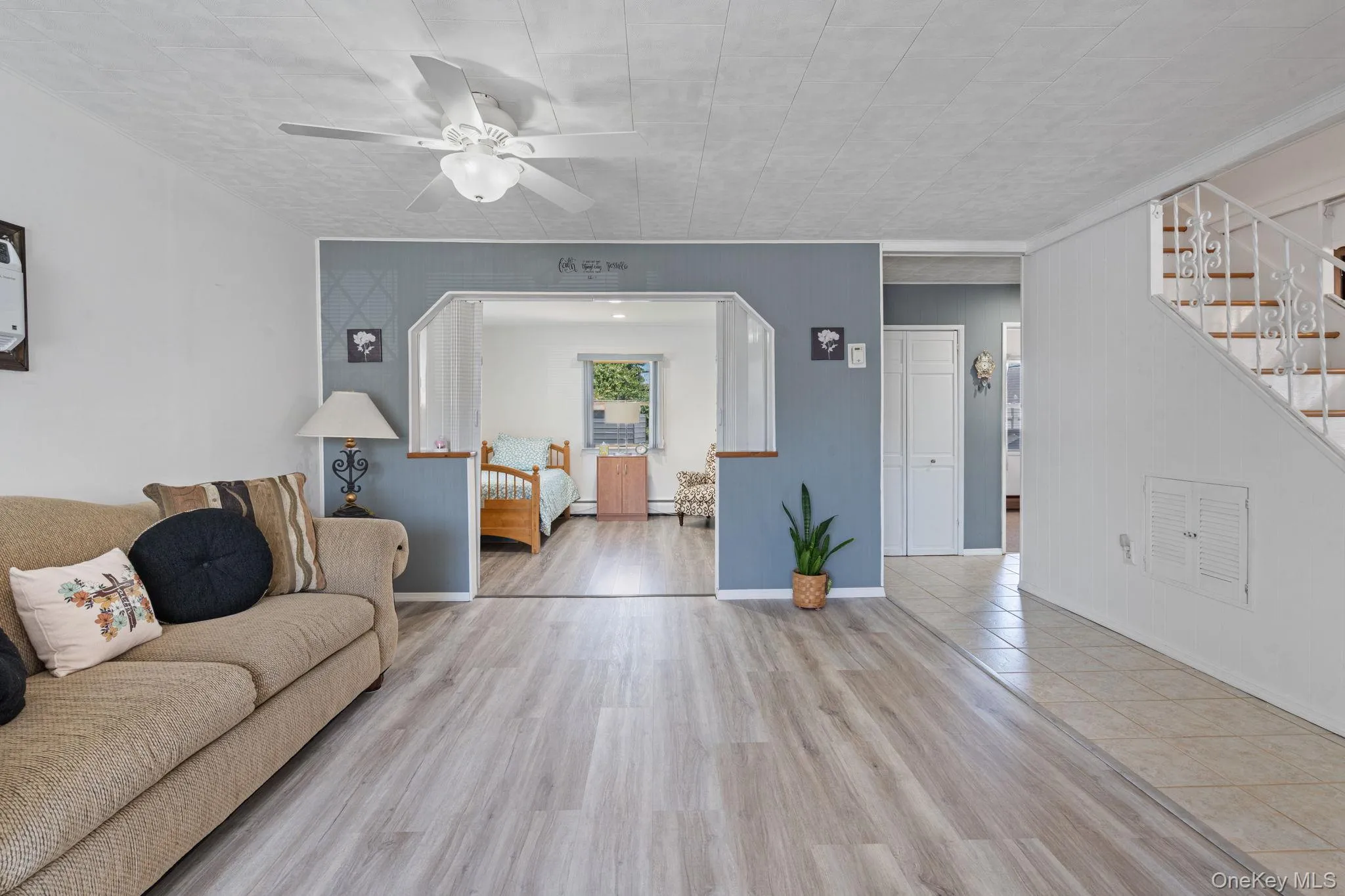 Bright living space featuring wood-finish flooring, a ceiling fan with integrated lighting, and a partial wall opening to an adjacent room Bright living space featuring wood-finish flooring, a ceiling fan with integrated lighting, and a partial wall opening to an adjacent room