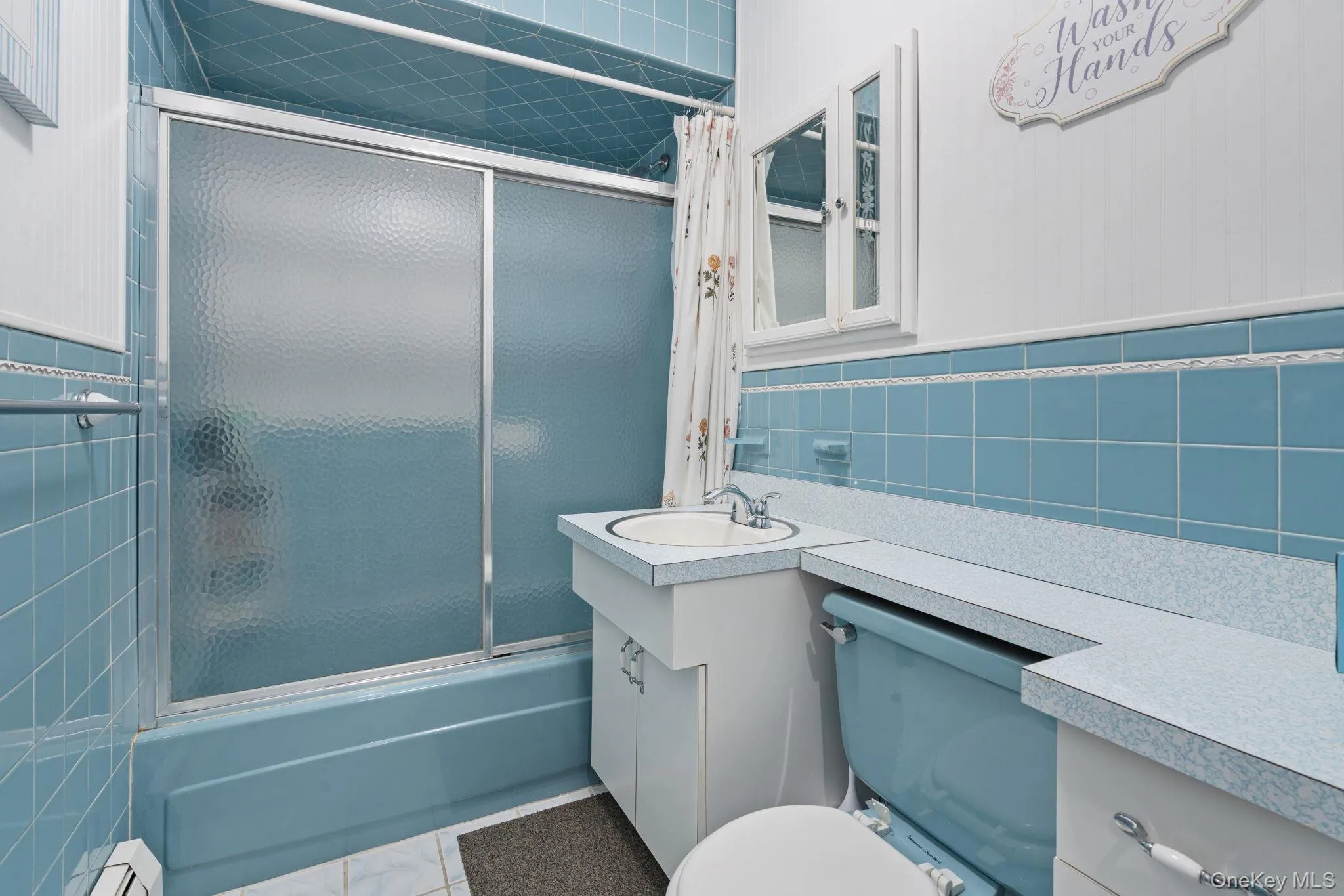 Full bath featuring a blue tiled shower/tub combination with sliding textured glass doors, a vanity with integrated sink, and an embedded medicine cabinet Full bath featuring a blue tiled shower/tub combination with sliding textured glass doors, a vanity with integrated sink, and an embedded medicine cabinet
