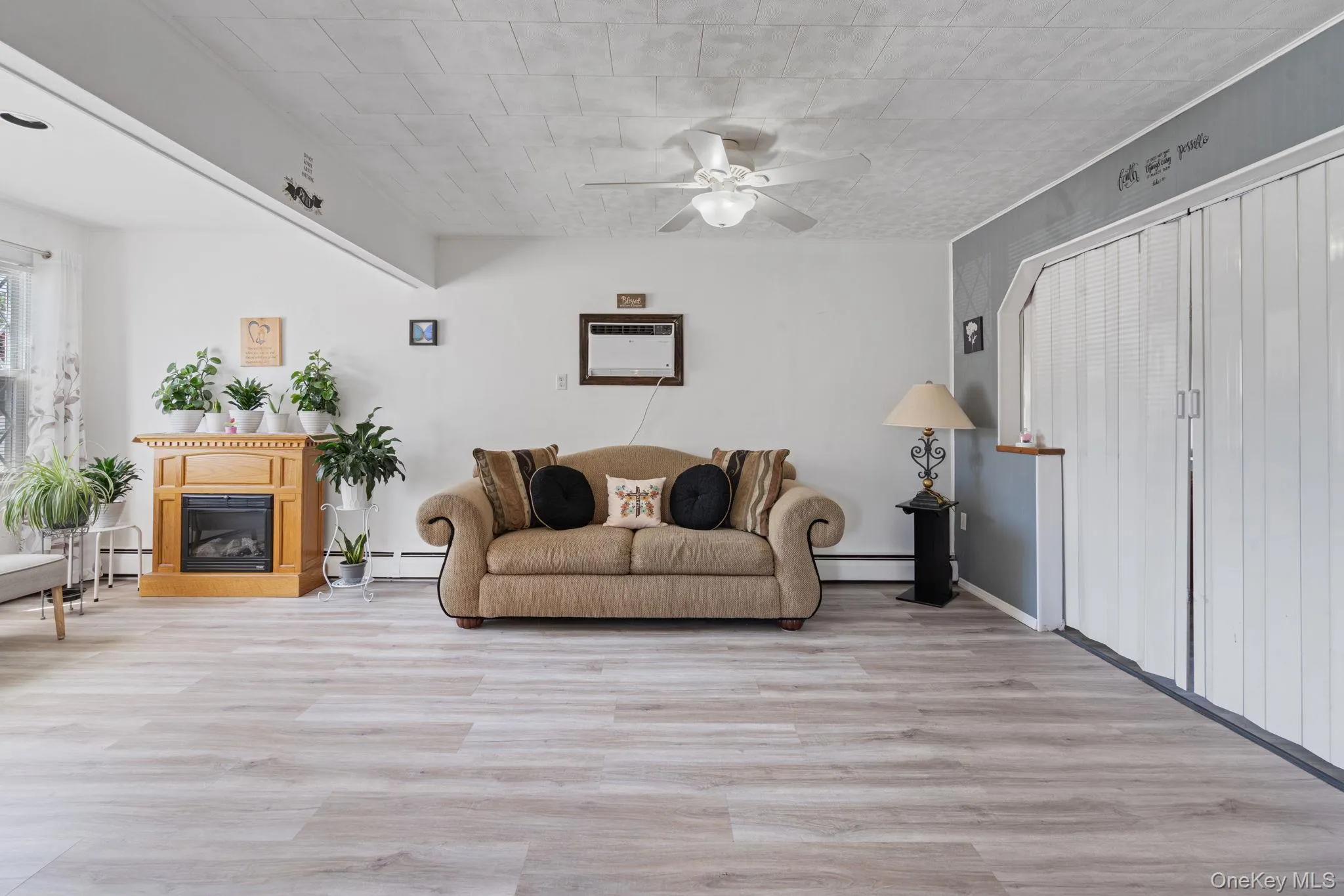 Bright living space featuring light wood-finish flooring, a ceiling fan, and an electric fireplace with a light wood mantel Bright living space featuring light wood-finish flooring, a ceiling fan, and an electric fireplace with a light wood mantel