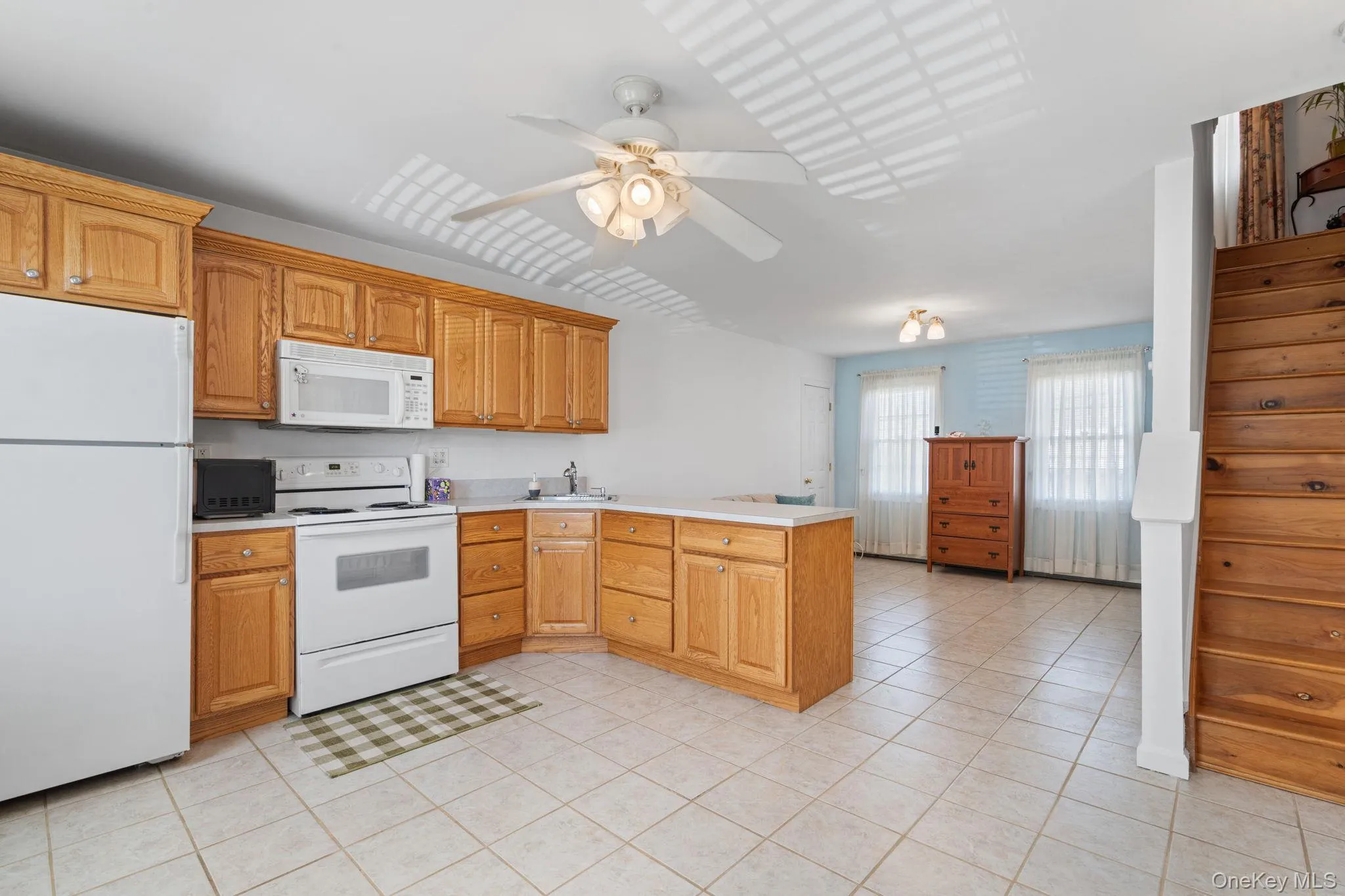 Kitchen featuring light wood cabinetry, white appliances, and a corner sink Kitchen featuring light wood cabinetry, white appliances, and a corner sink