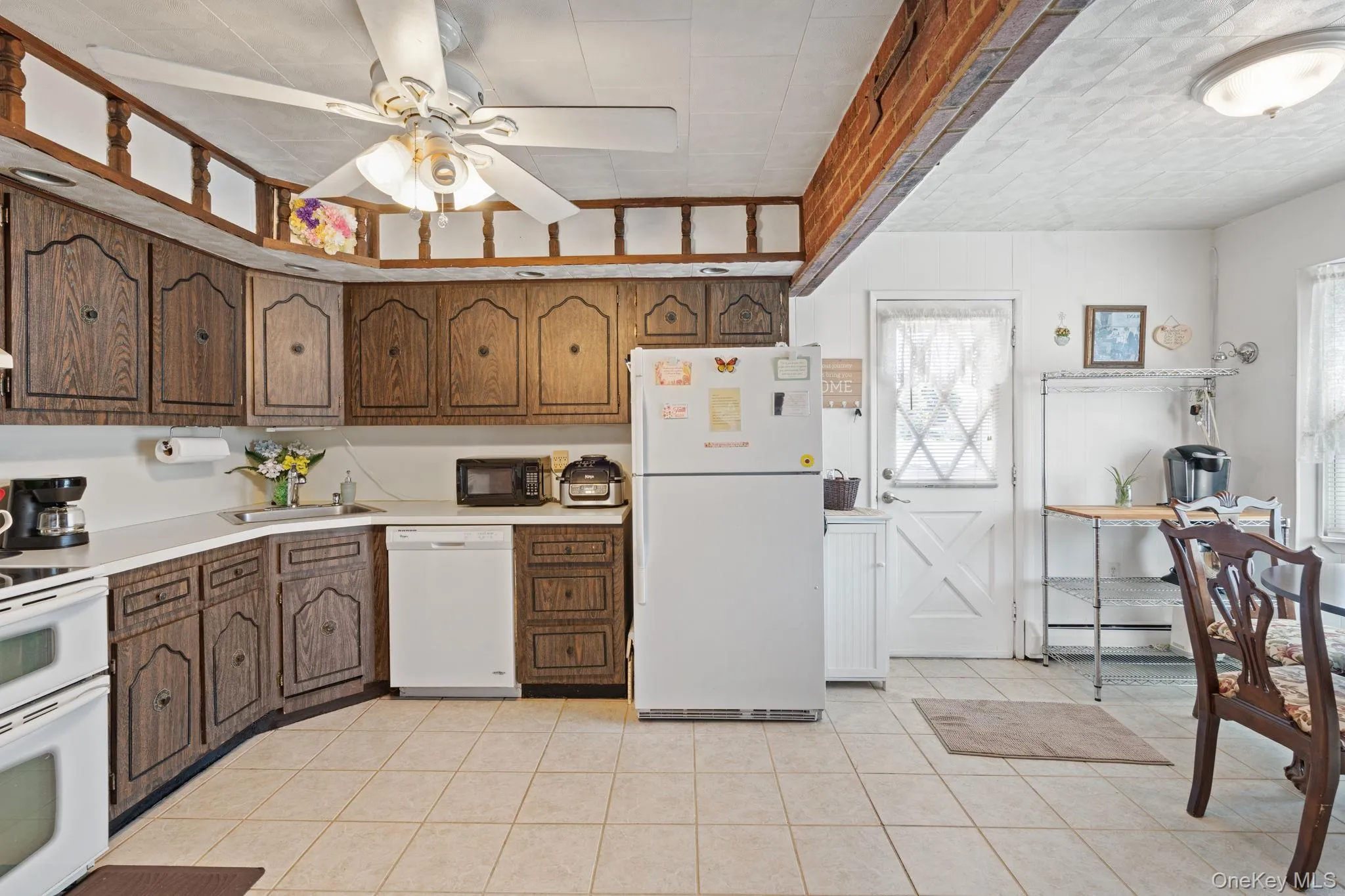 Kitchen featuring wood-finish cabinetry, white countertops, tile flooring, and a white ceiling fan with integrated lighting Kitchen featuring wood-finish cabinetry, white countertops, tile flooring, and a white ceiling fan with integrated lighting