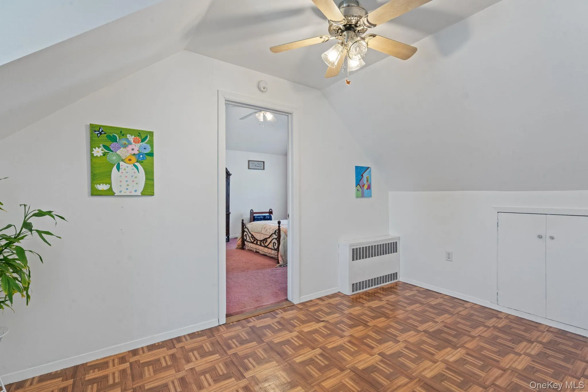 Attic room featuring parquet wood-finish flooring, a ceiling fan with light fixture, and built-in storage cabinets Attic room featuring parquet wood-finish flooring, a ceiling fan with light fixture, and built-in storage cabinets