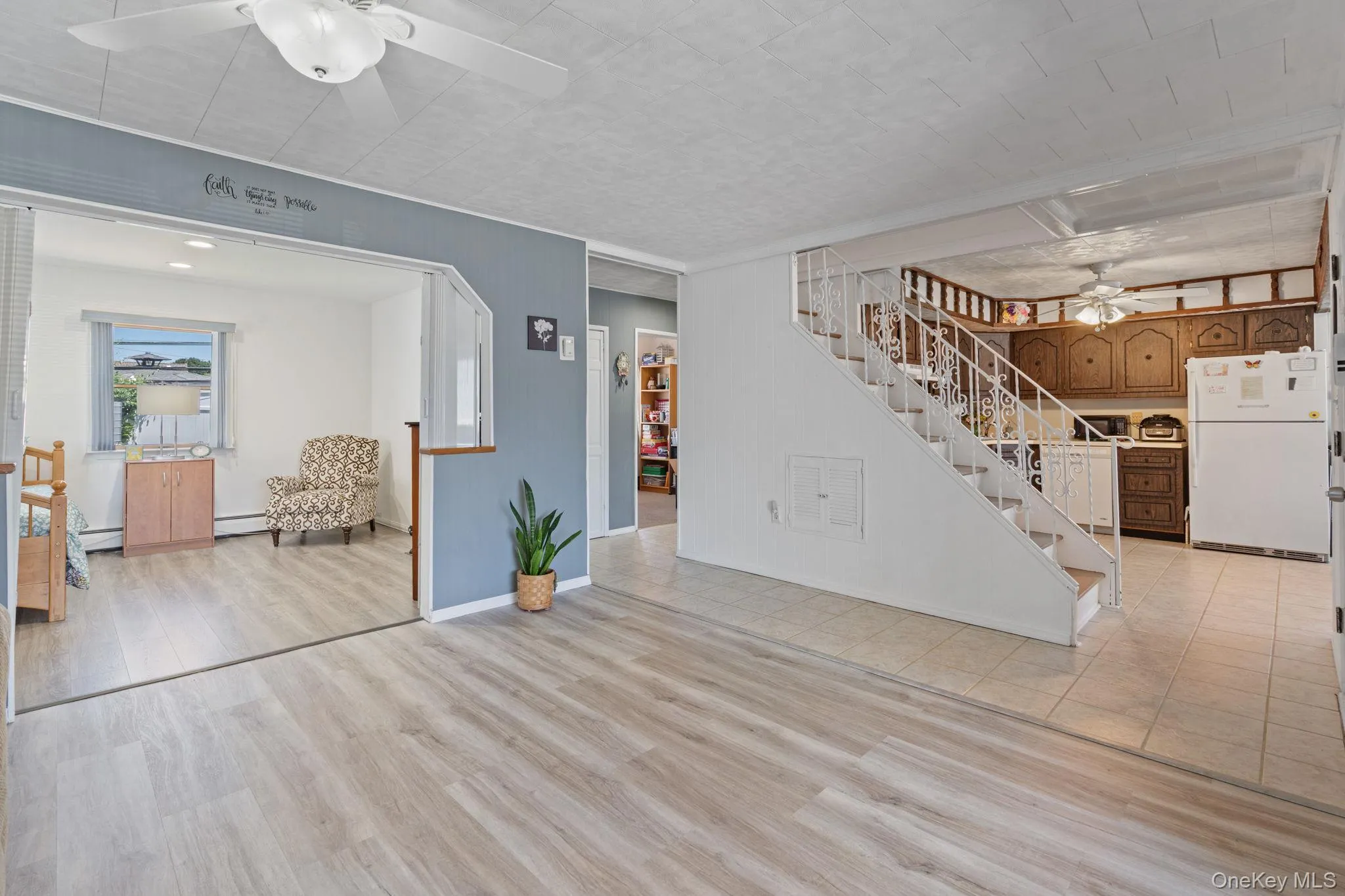 Open concept living space featuring wood-finish flooring, a white ceiling fan, and a wide entryway to an additional room Open concept living space featuring wood-finish flooring, a white ceiling fan, and a wide entryway to an additional room