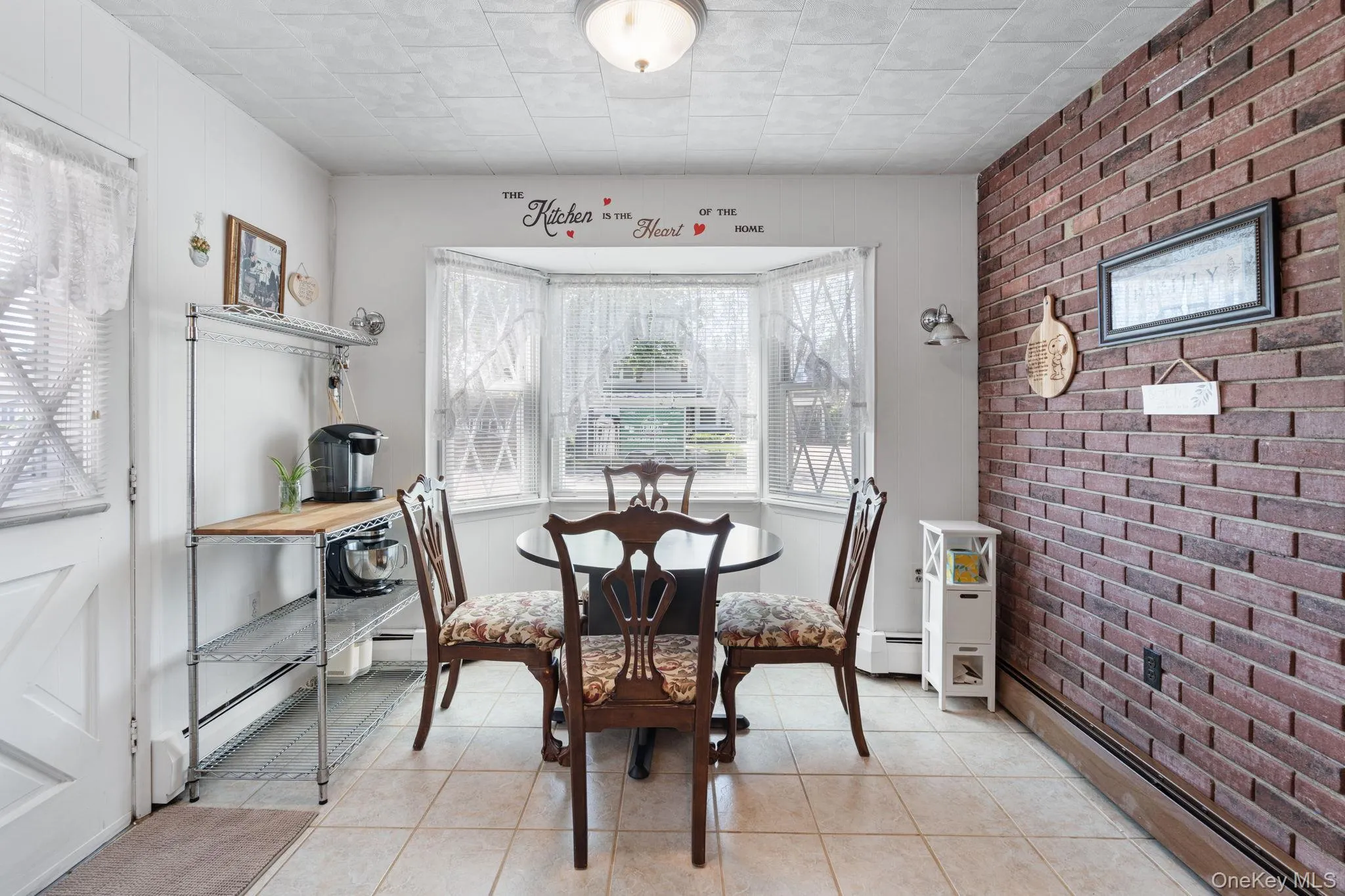 Dining area featuring a bay window, brick accent wall, tiled flooring, and a white paneled door Dining area featuring a bay window, brick accent wall, tiled flooring, and a white paneled door
