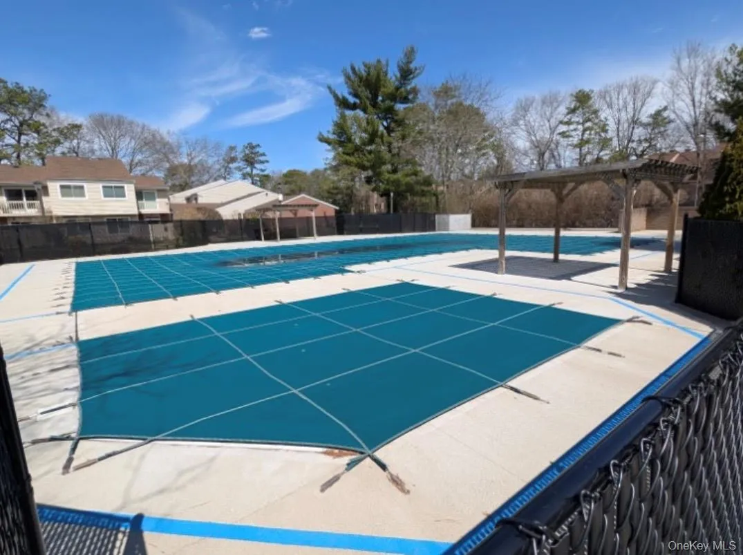 Outdoor aquatic area featuring multiple covered pools, a wood pergola, and a black chain-link fence Outdoor aquatic area featuring multiple covered pools, a wood pergola, and a black chain-link fence
