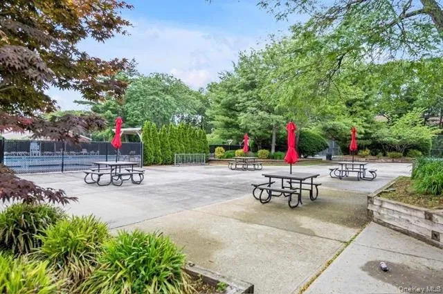 Paved patio area featuring multiple picnic tables with umbrellas, surrounded by mature trees and landscaping Paved patio area featuring multiple picnic tables with umbrellas, surrounded by mature trees and landscaping