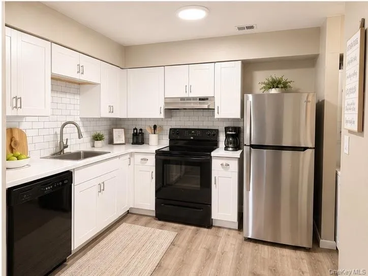 Kitchen with light-finish flooring, white cabinetry, a subway backsplash, and stainless steel appliances Kitchen with light-finish flooring, white cabinetry, a subway backsplash, and stainless steel appliances
