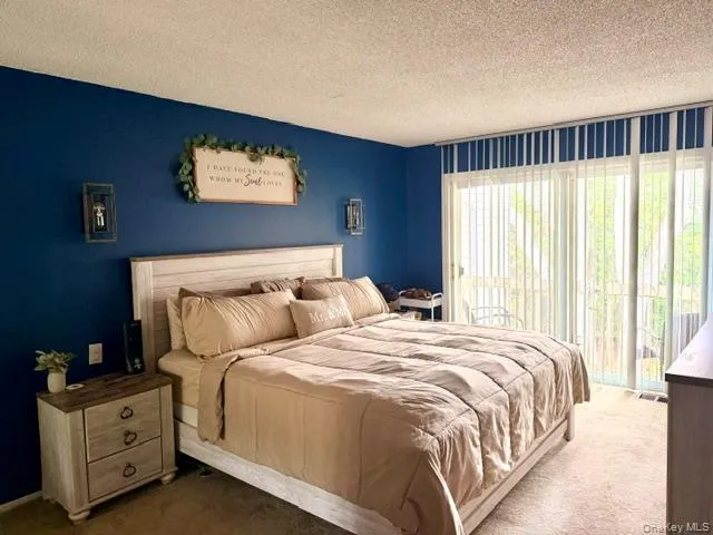 Bedroom featuring vibrant blue wall accent, neutral carpeting, and a sliding glass door with vertical blinds providing access to an exterior space Bedroom featuring vibrant blue wall accent, neutral carpeting, and a sliding glass door with vertical blinds providing access to an exterior space