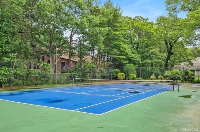 On-property tennis court featuring a blue playing surface with green perimeter and white boundary lines, surrounded by mature trees On-property tennis court featuring a blue playing surface with green perimeter and white boundary lines, surrounded by mature trees