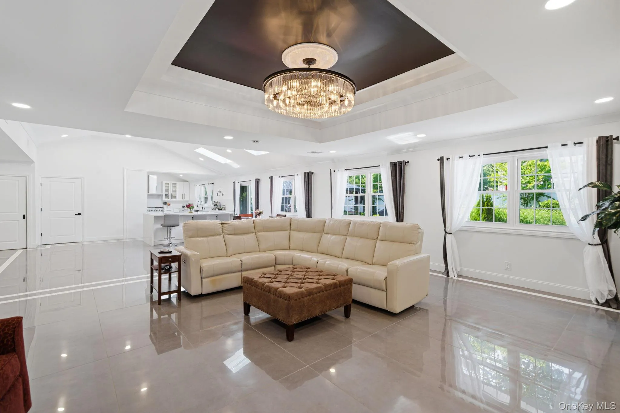 Open and bright living room with decorative ceiling, stunning chandelier, recessed lighting, wall of windows, electric fireplace and porcelain tile floors. Open and bright living room with decorative ceiling, stunning chandelier, recessed lighting, wall of windows, electric fireplace and porcelain tile floors.