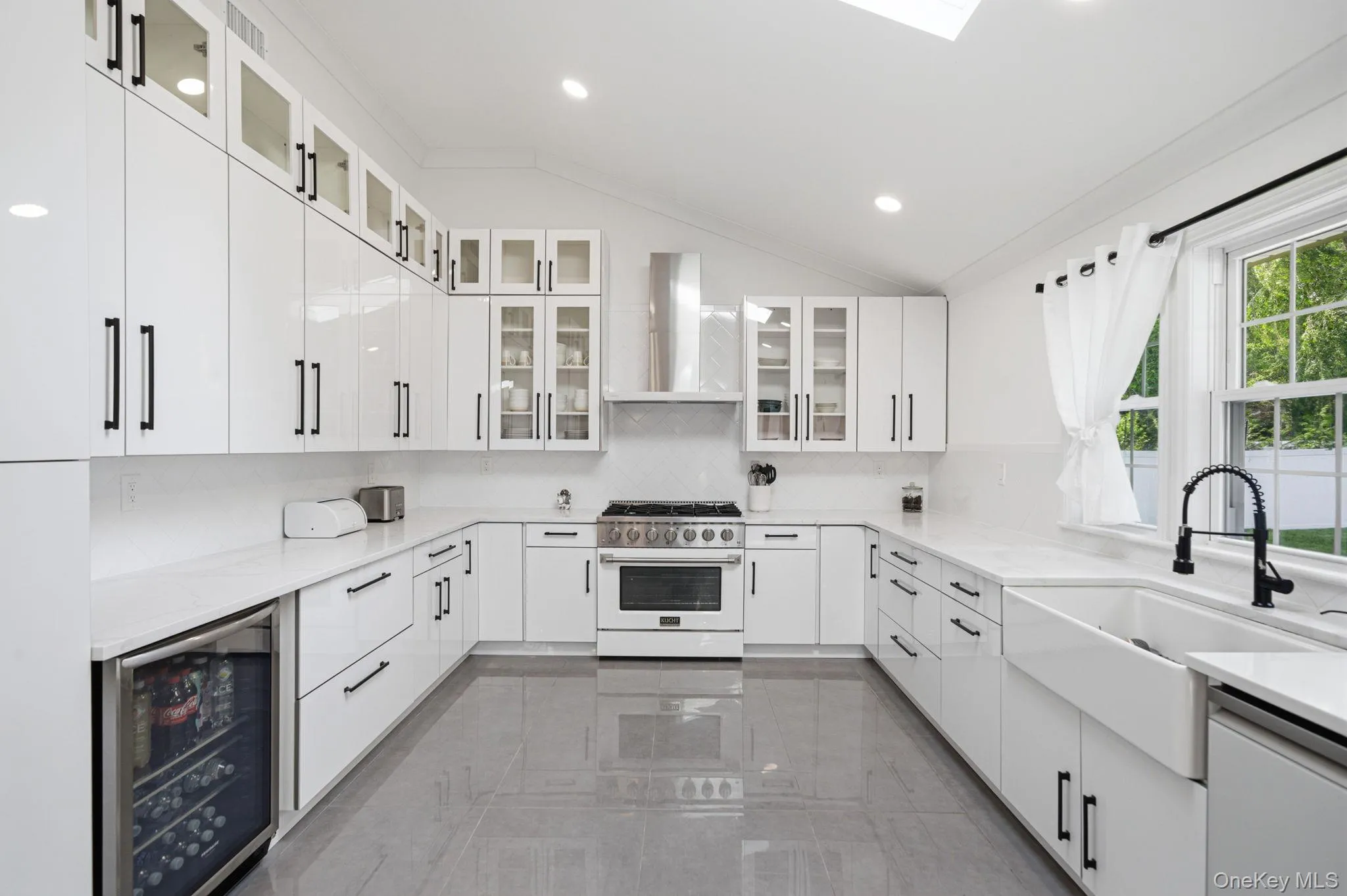 Bright and open renovated kitchen. Endless white cabinets and counter space. High end white appliances including natural gas cooking and a mini drink refrigerator. Farm sink, skylight, recessed lighting, and porcelain tile flooring. Bright and open renovated kitchen. Endless white cabinets and counter space. High end white appliances including natural gas cooking and a mini drink refrigerator. Farm sink, skylight, recessed lighting, and porcelain tile flooring.