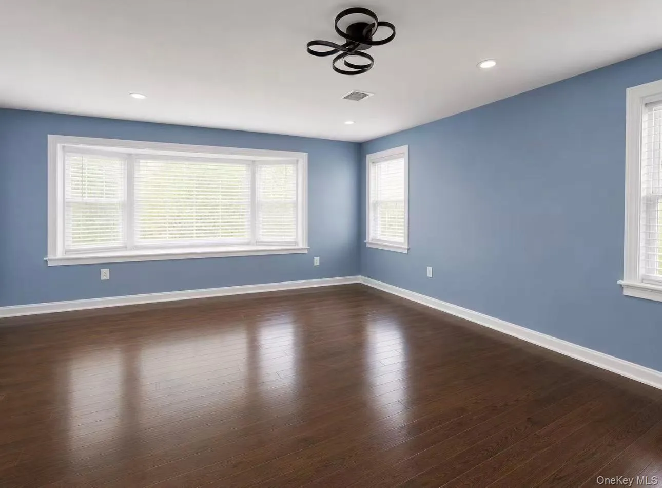 Spacious room with dark wood-finish flooring, white baseboards, and light blue walls Spacious room with dark wood-finish flooring, white baseboards, and light blue walls