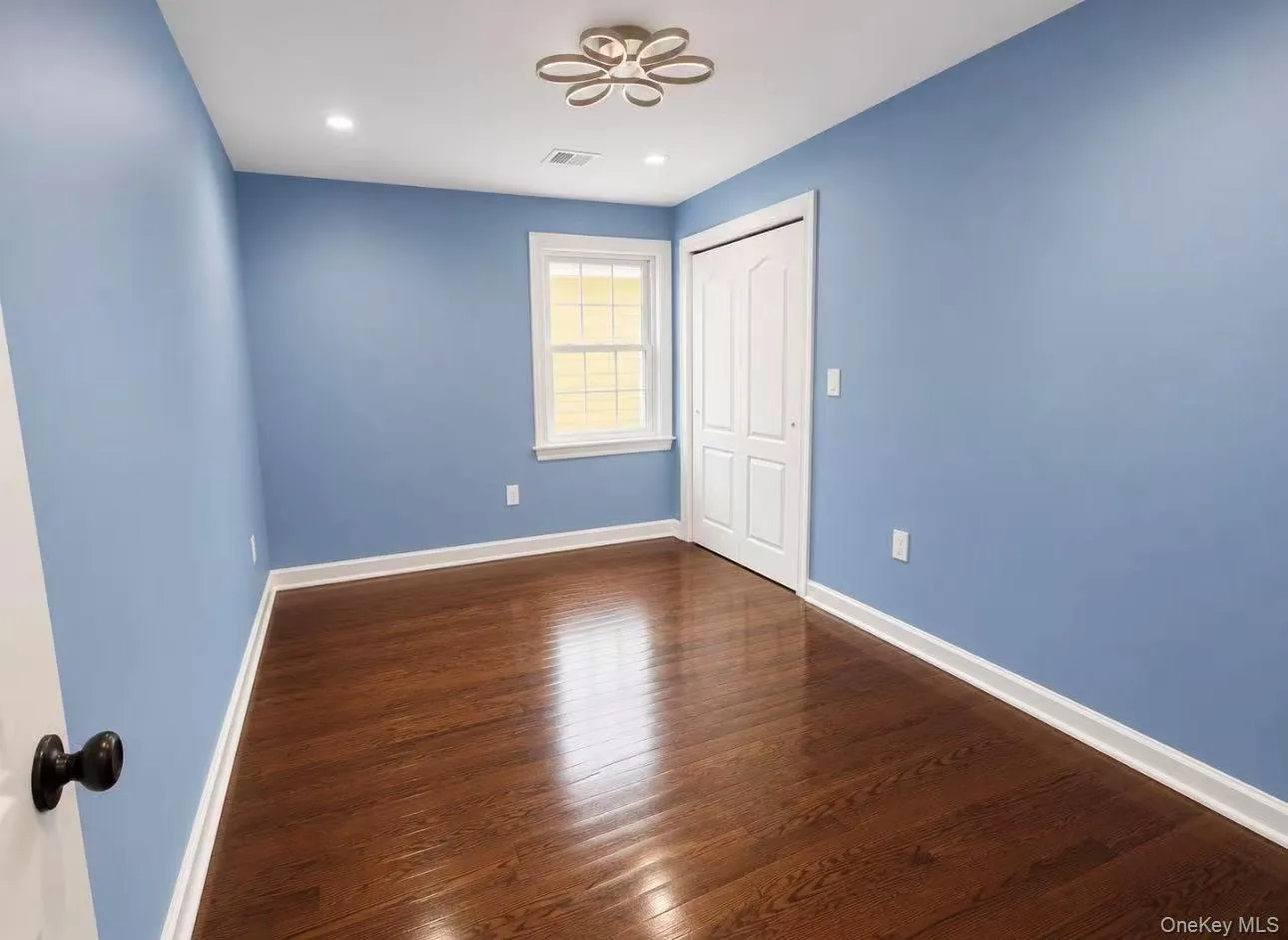 Interior room featuring wood-finish flooring and a contemporary ceiling light fixture Interior room featuring wood-finish flooring and a contemporary ceiling light fixture