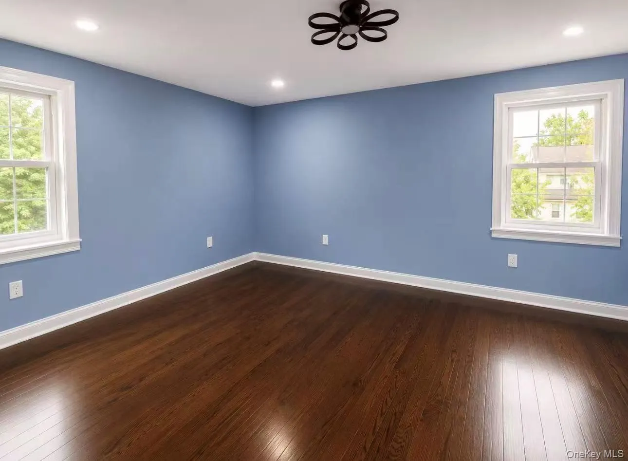 Spacious room featuring wood-finish flooring, two windows with white trim, recessed lighting, and a modern ceiling fixture Spacious room featuring wood-finish flooring, two windows with white trim, recessed lighting, and a modern ceiling fixture