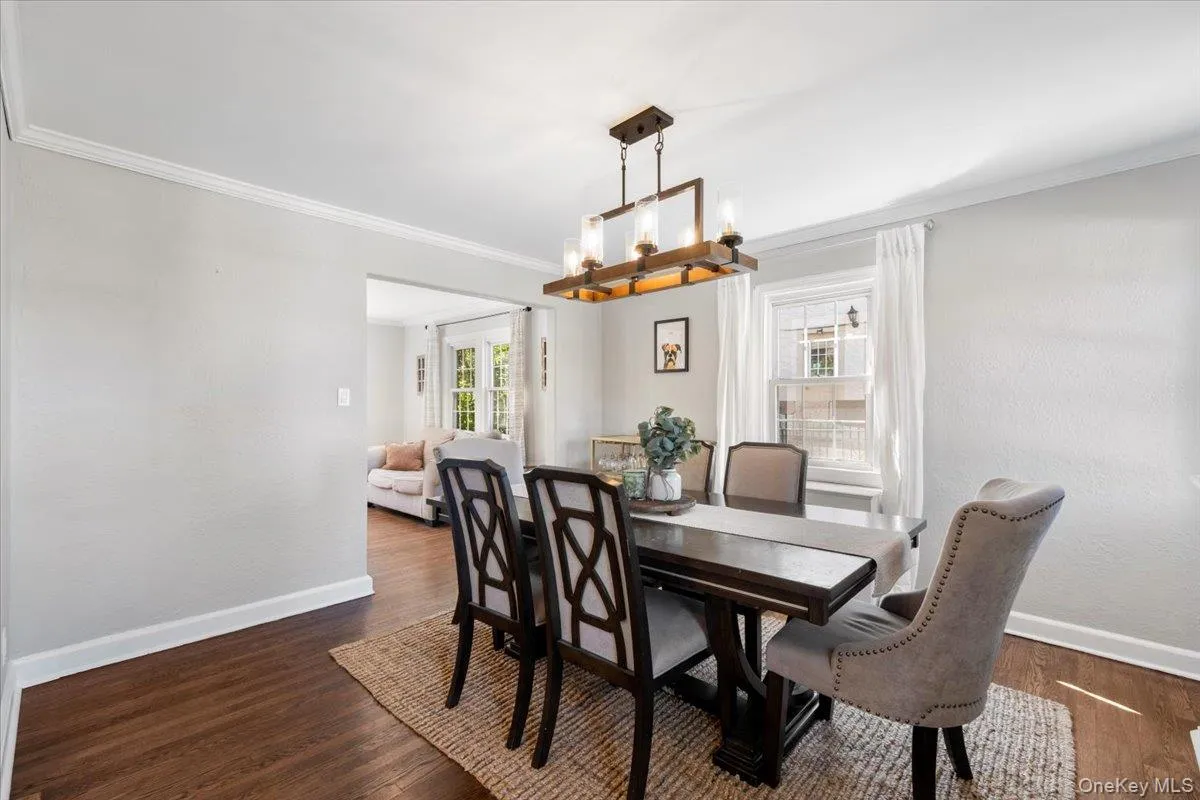 Dining area featuring wood-finish flooring, a rectangular light fixture, crown molding, and a window with white trim Dining area featuring wood-finish flooring, a rectangular light fixture, crown molding, and a window with white trim