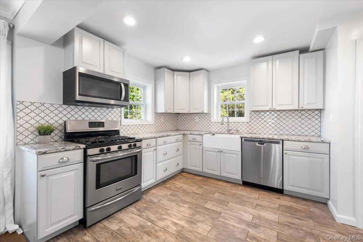 Kitchen featuring wood-finish flooring, white shaker-style cabinetry, granite countertops, and a white arabesque tile backsplash Kitchen featuring wood-finish flooring, white shaker-style cabinetry, granite countertops, and a white arabesque tile backsplash