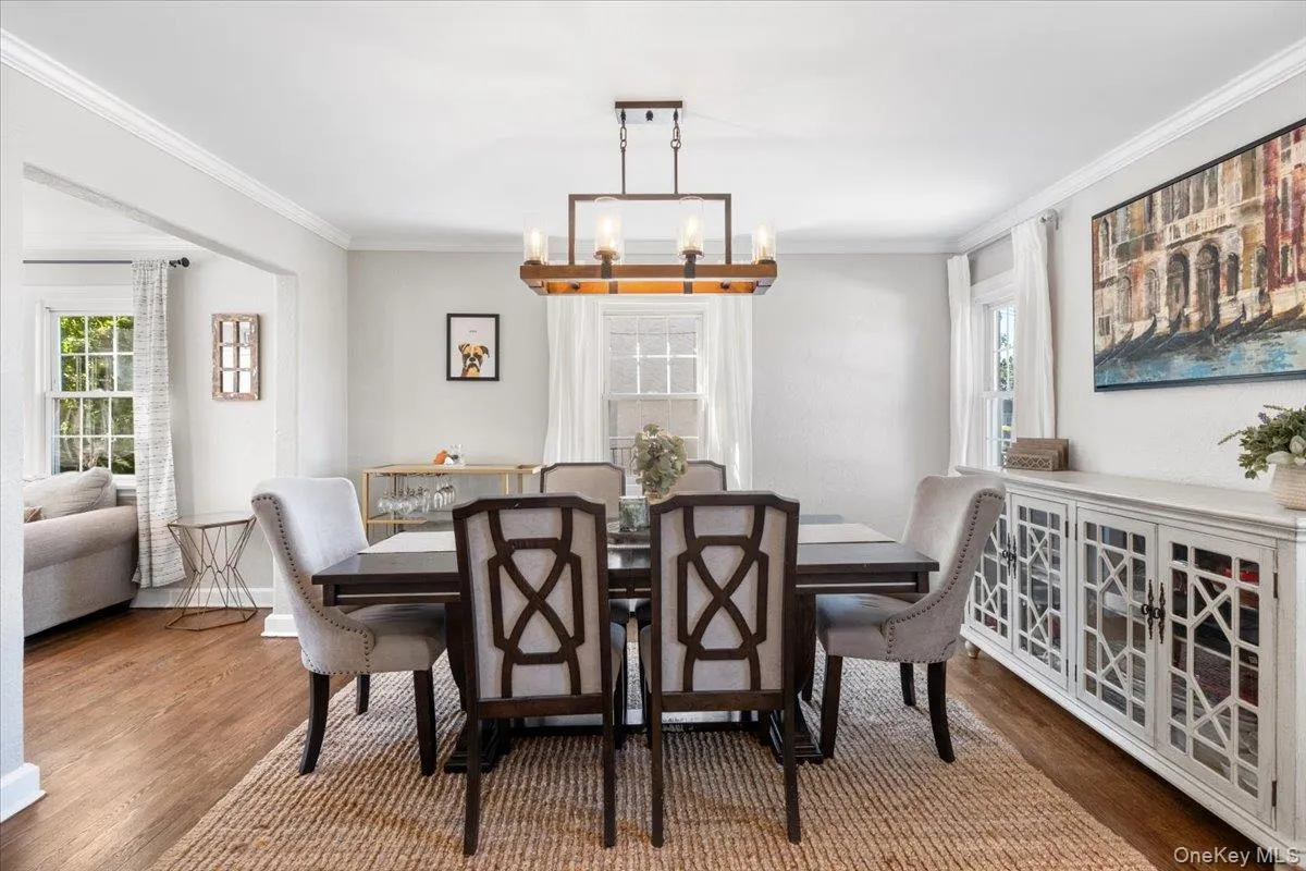 Dining area featuring wood-finish flooring, a rectangular chandelier, crown molding, and a built-in white buffet cabinet with geometric glass panels Dining area featuring wood-finish flooring, a rectangular chandelier, crown molding, and a built-in white buffet cabinet with geometric glass panels