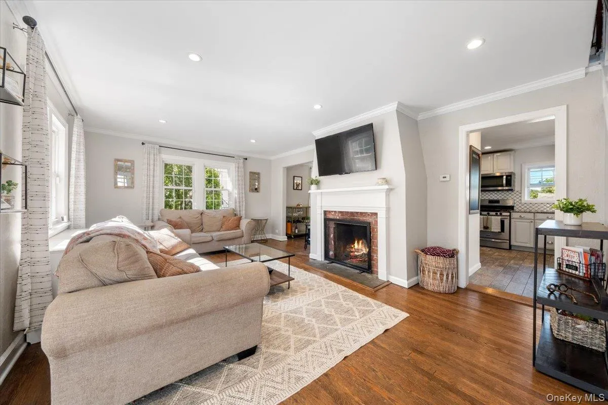 Living area featuring rich wood-finish flooring, recessed lighting, and a fireplace with a brick surround and white mantel Living area featuring rich wood-finish flooring, recessed lighting, and a fireplace with a brick surround and white mantel