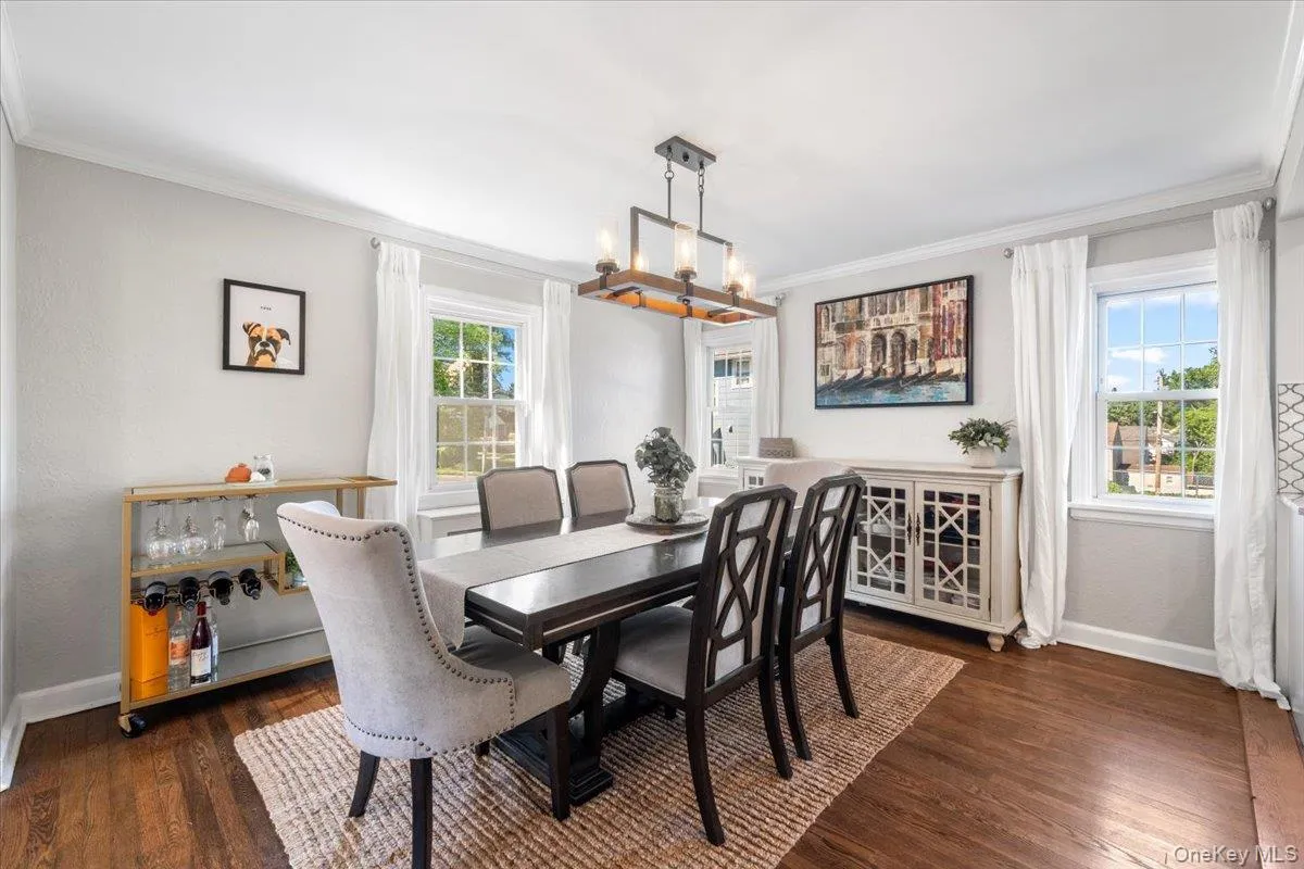 Dining area featuring wood-finish flooring, a rectangular dining table, and a linear chandelier with exposed bulbs Dining area featuring wood-finish flooring, a rectangular dining table, and a linear chandelier with exposed bulbs