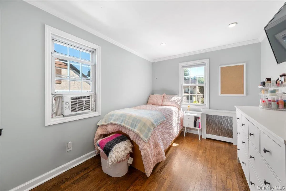 Room featuring wood-finish flooring, two windows with white trim, and light gray wall paint Room featuring wood-finish flooring, two windows with white trim, and light gray wall paint